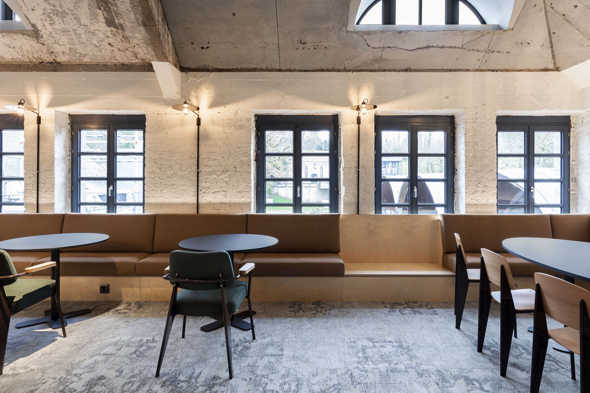 Seating area with continuous tan upholstered benches below a row of dark steel-framed windows