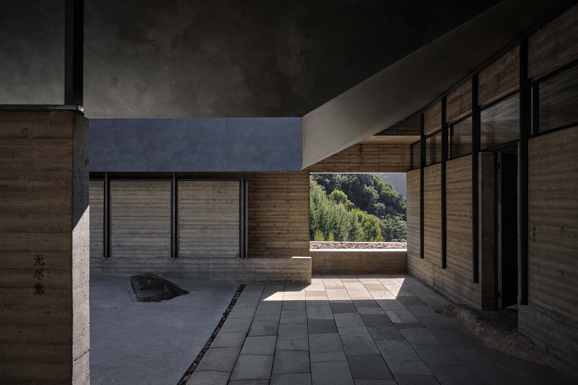 Interior courtyard with rammed earth walls, dark paving and a single boulder under filtered daylight