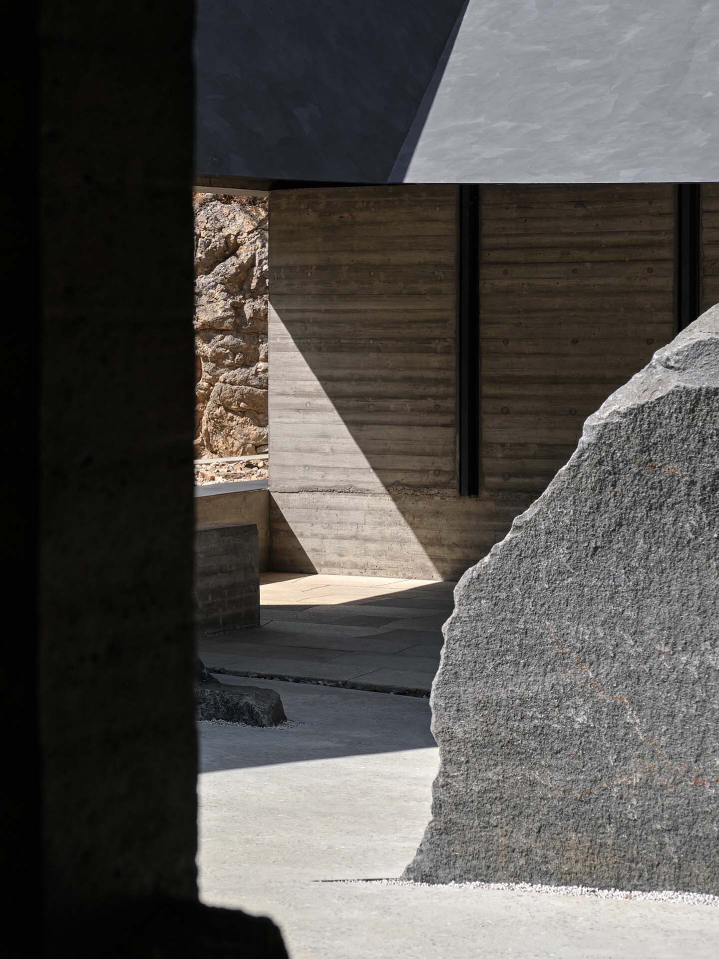 Sunlit courtyard corner framed by shadow with boulder and timber formwork wall in bright light