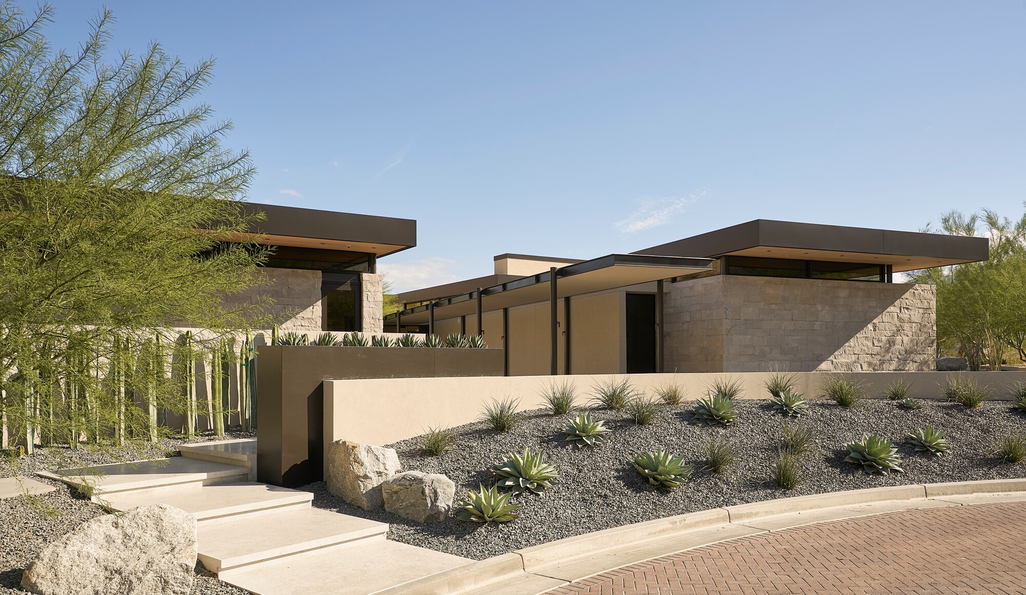 Entry approach showing stucco and stone volumes with cantilevered roofs in desert setting