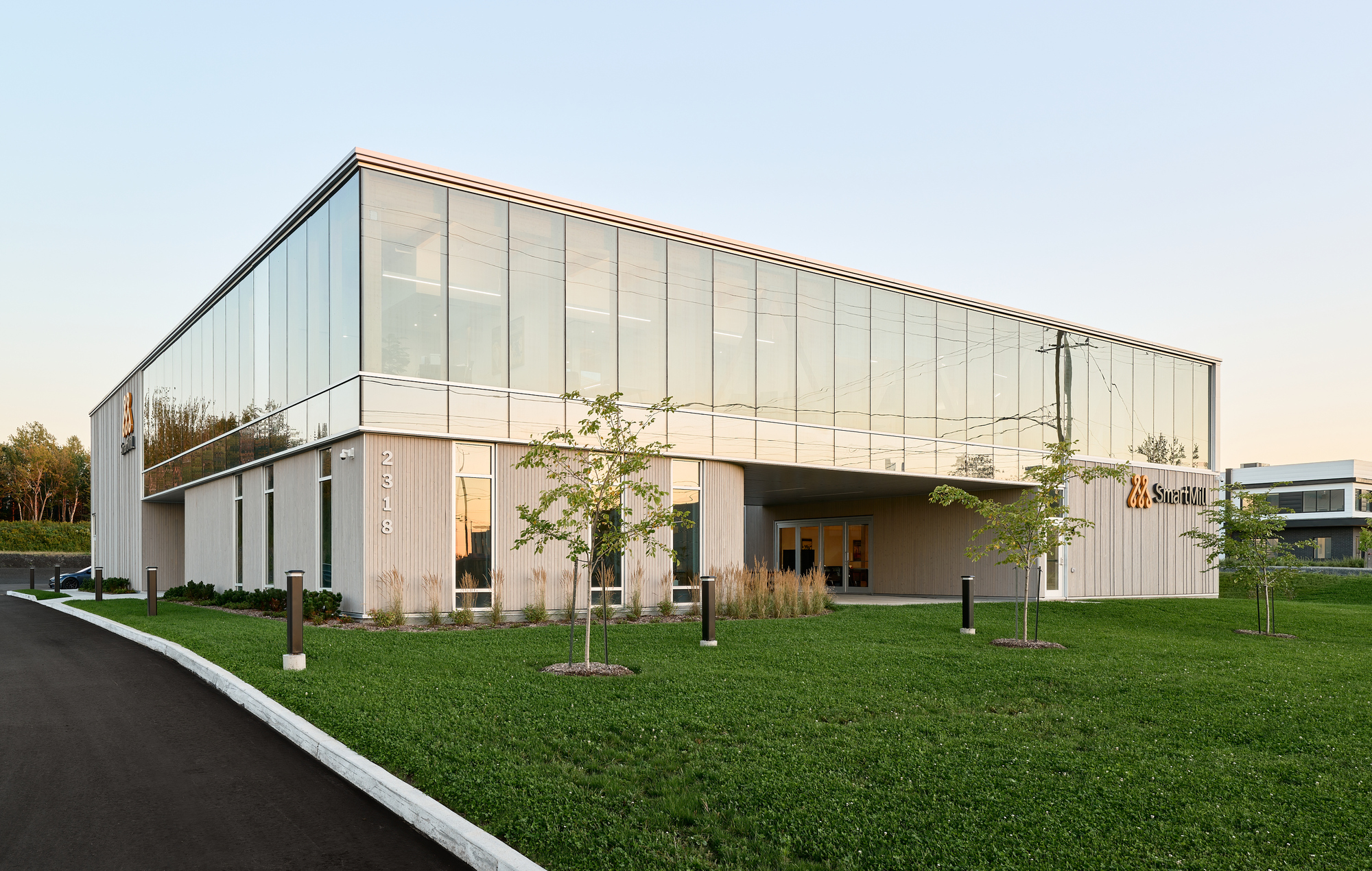Vertical metal panel and glass facade with young trees planted in a lawn at dusk
