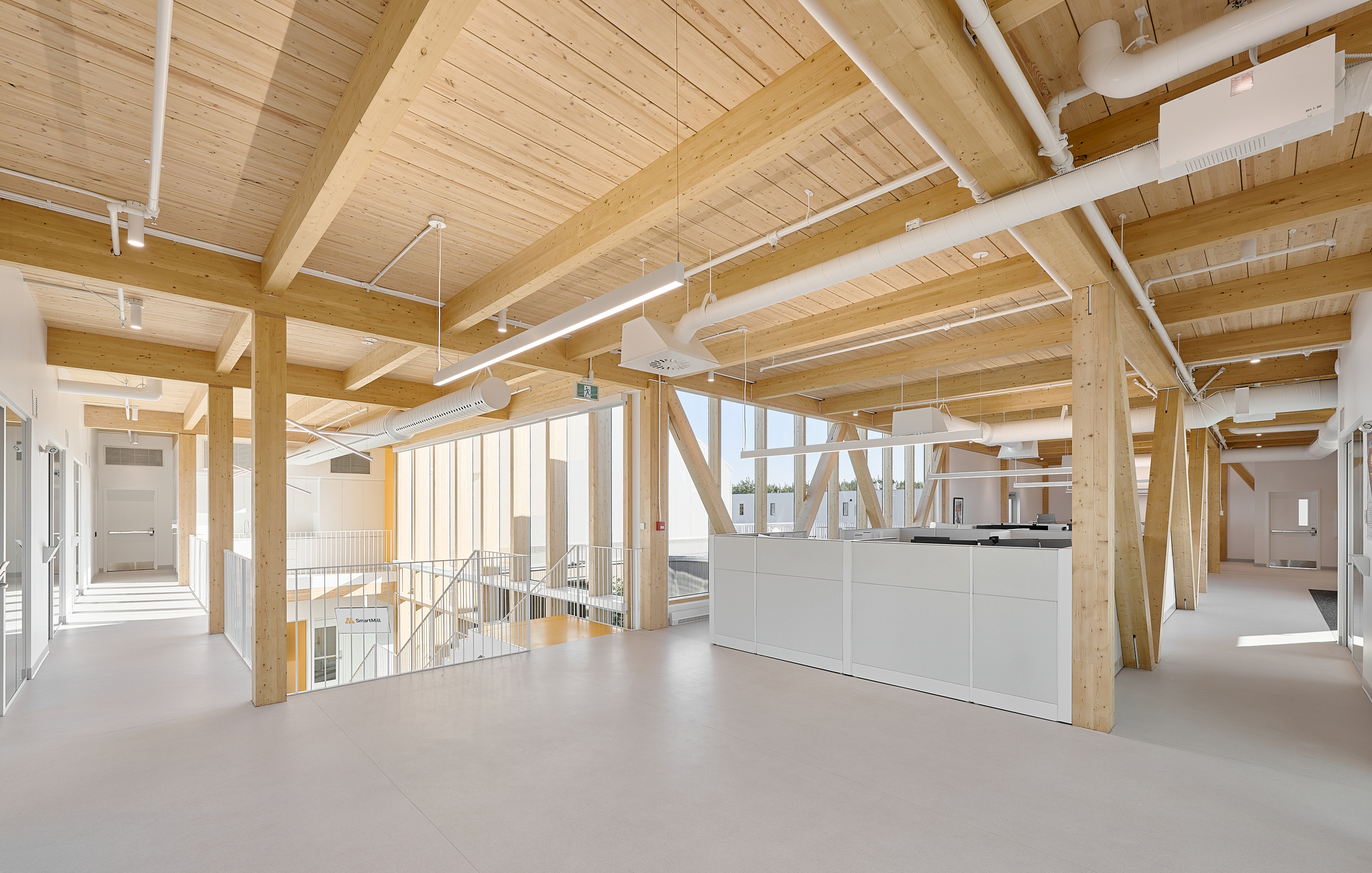 Upper-level open workspace with exposed timber beams and a white central millwork unit overlooking the floor below