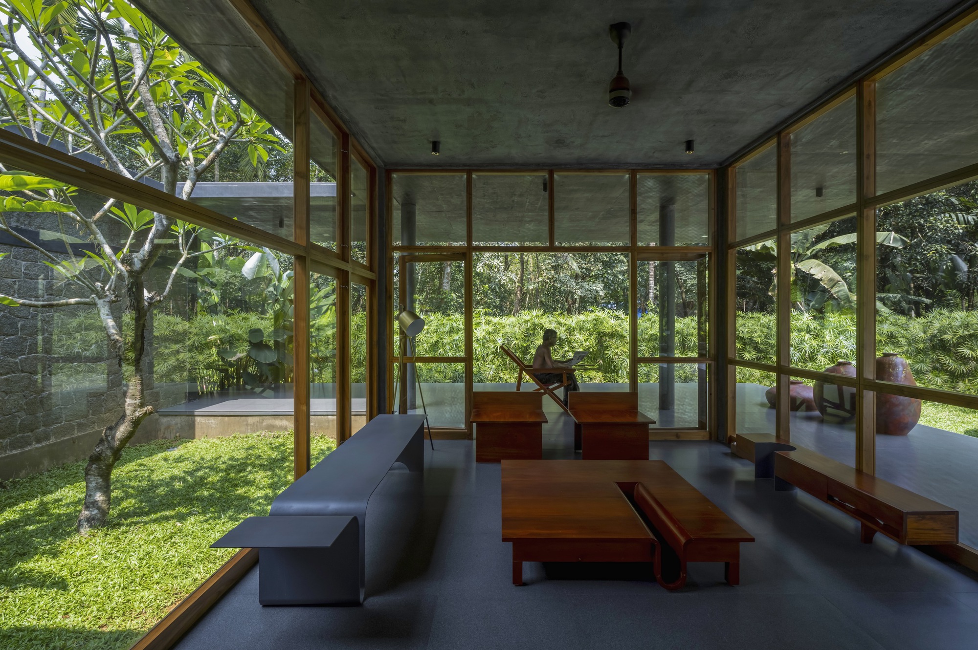 Living room with floor-to-ceiling timber-framed glazing opening onto a lawn with two seated figures beyond