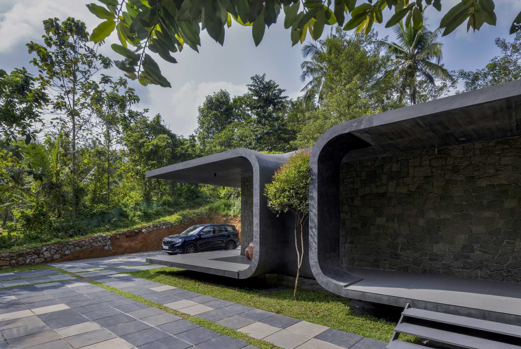 Curved concrete carport canopy with planted green roof sheltering a vehicle under cloudy skies