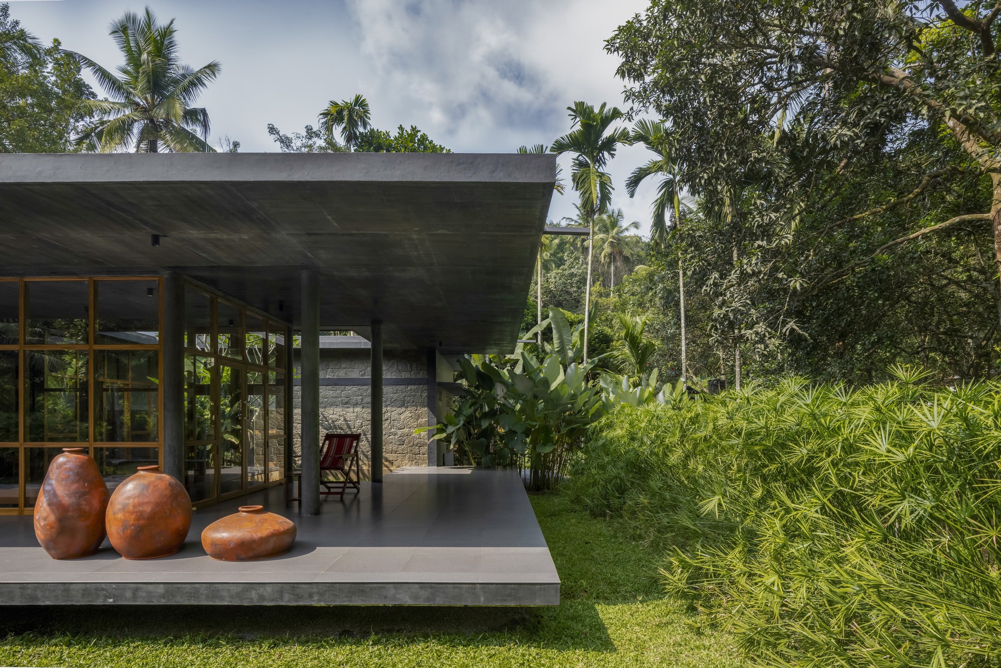 Covered terrace with concrete slab floor displaying three ceramic vessels alongside banana plants and palms