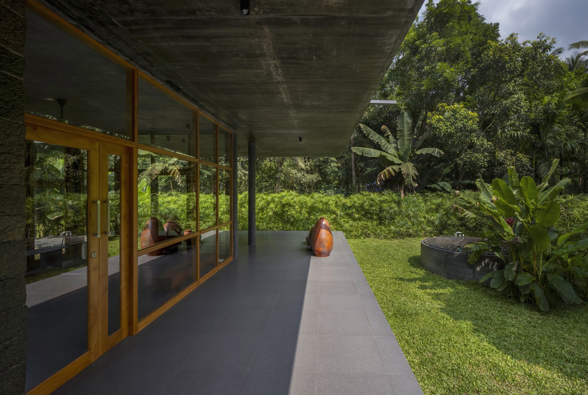 Concrete overhang sheltering a walkway with timber framed glazing overlooking a lawn and banana plants