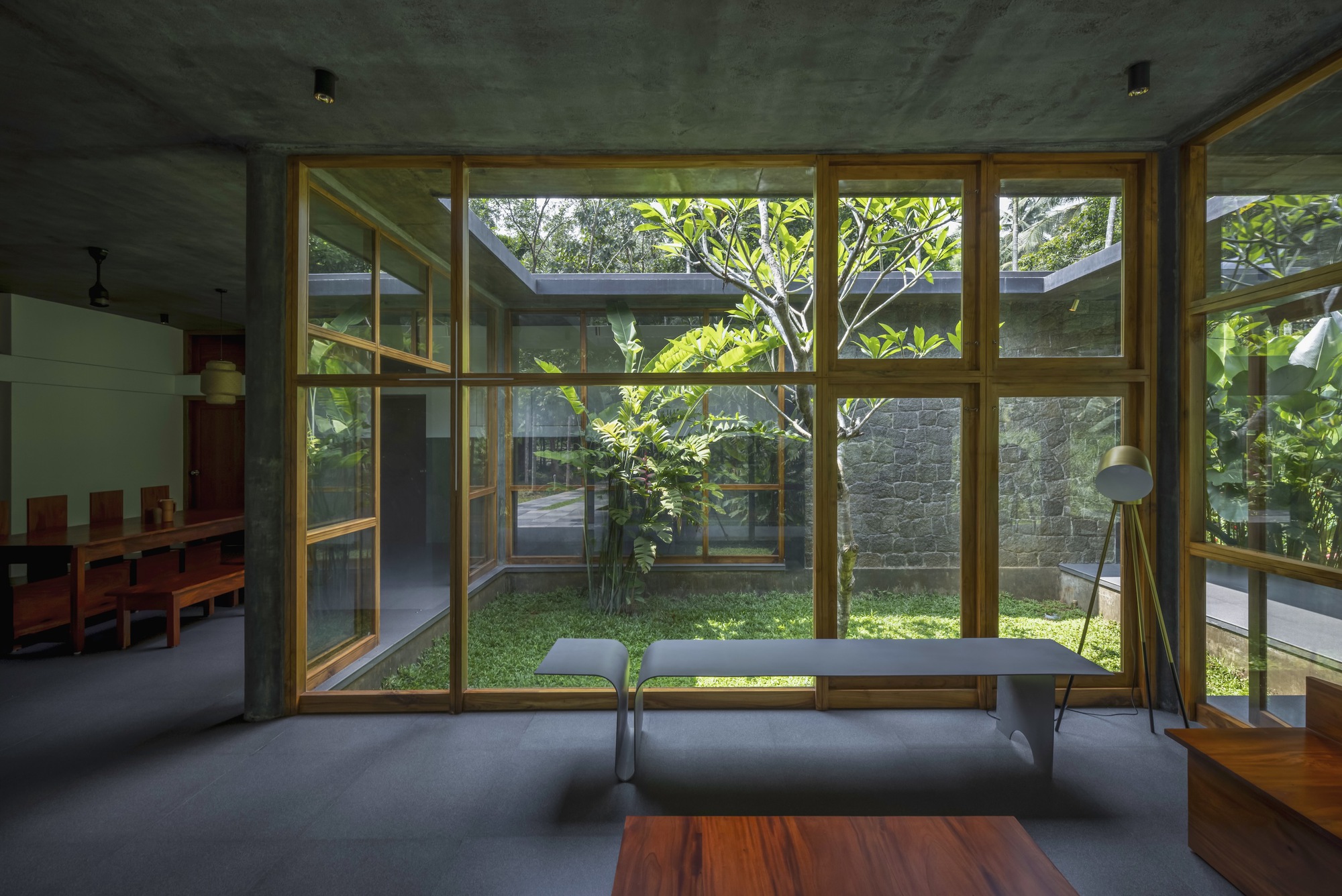 Interior view through timber window wall to courtyard with tree and stone wall beyond