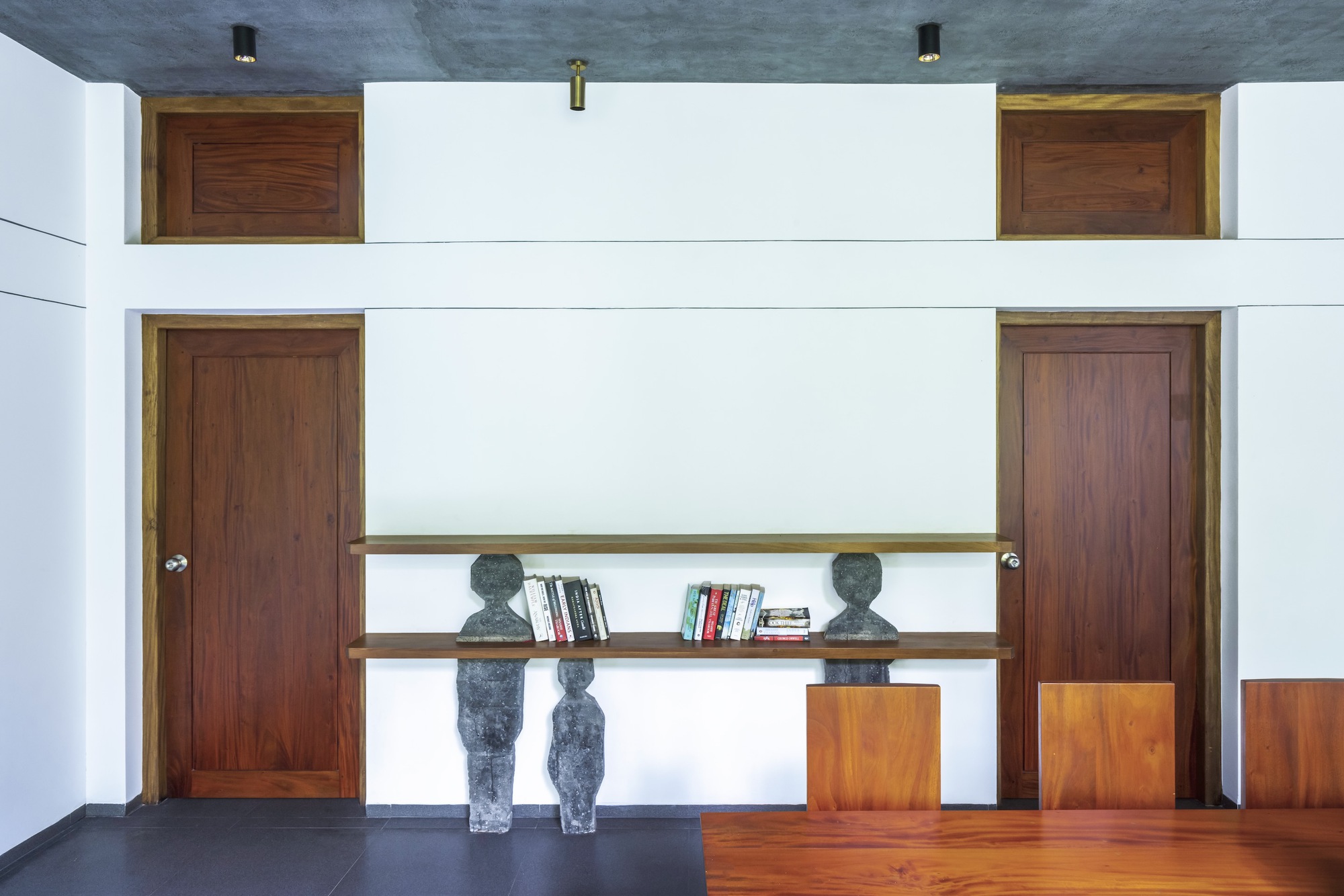 Double-height interior wall with symmetrical timber doors and suspended bookshelves flanked by two sculptures