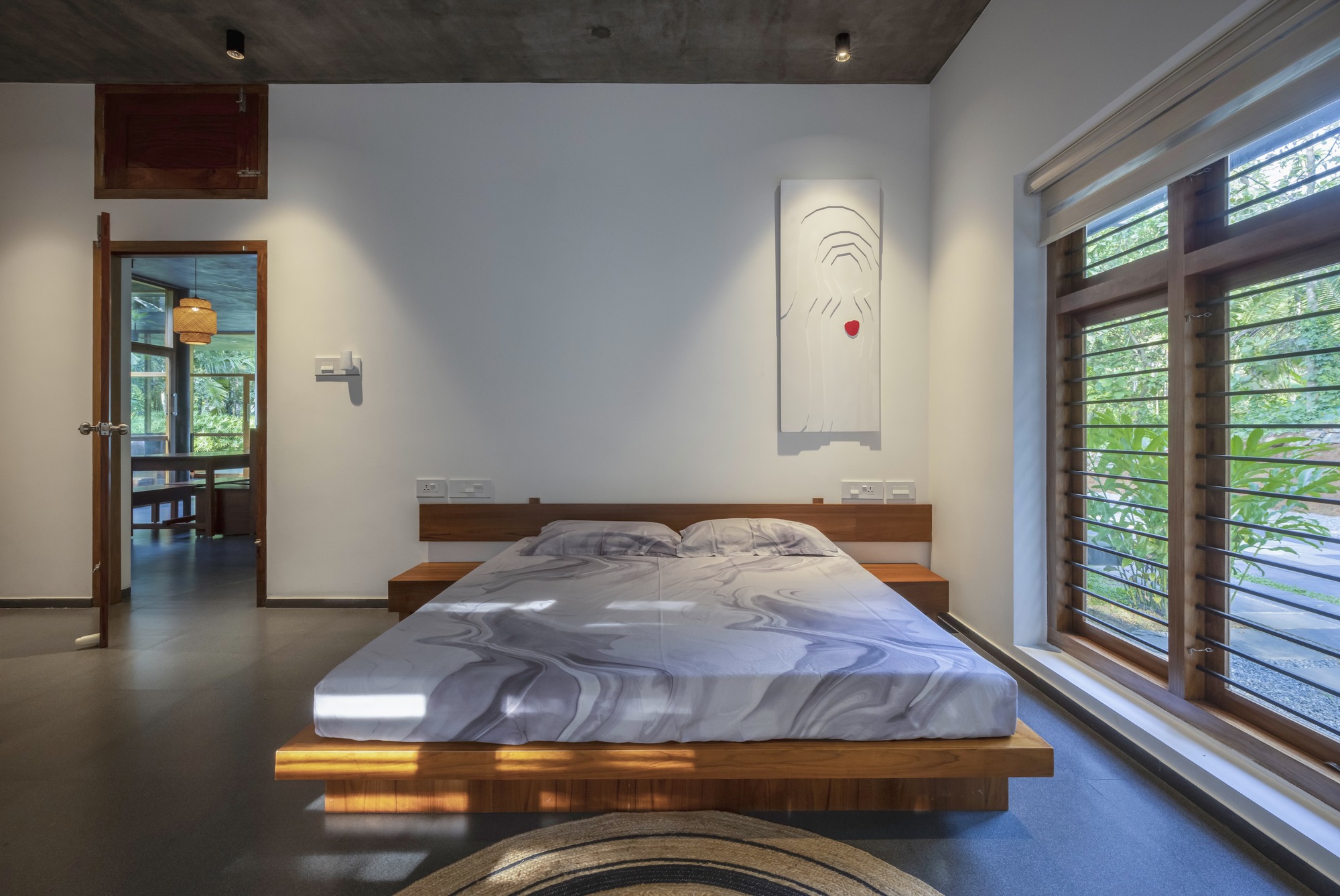 Bedroom with platform bed and horizontal louvered windows casting striped sunlight across the floor