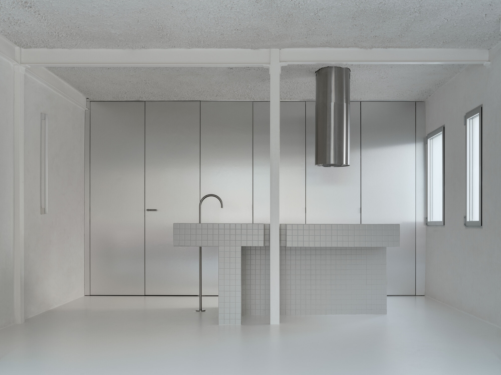 Open kitchen with white mosaic tile island, cylindrical steel range hood and brushed steel cabinet wall