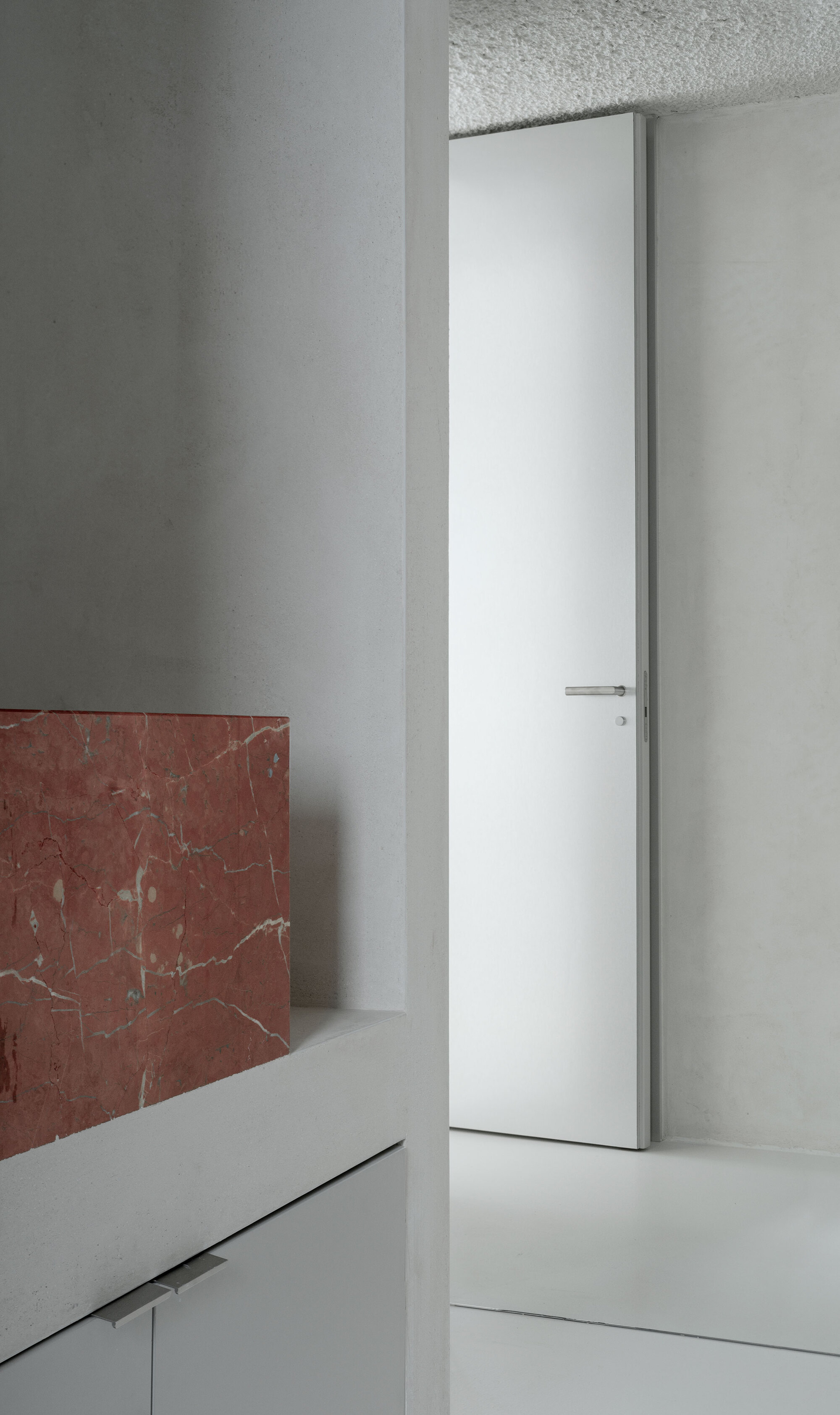 White flush door set into plaster walls with red marble wainscoting and terrazzo ceiling panel