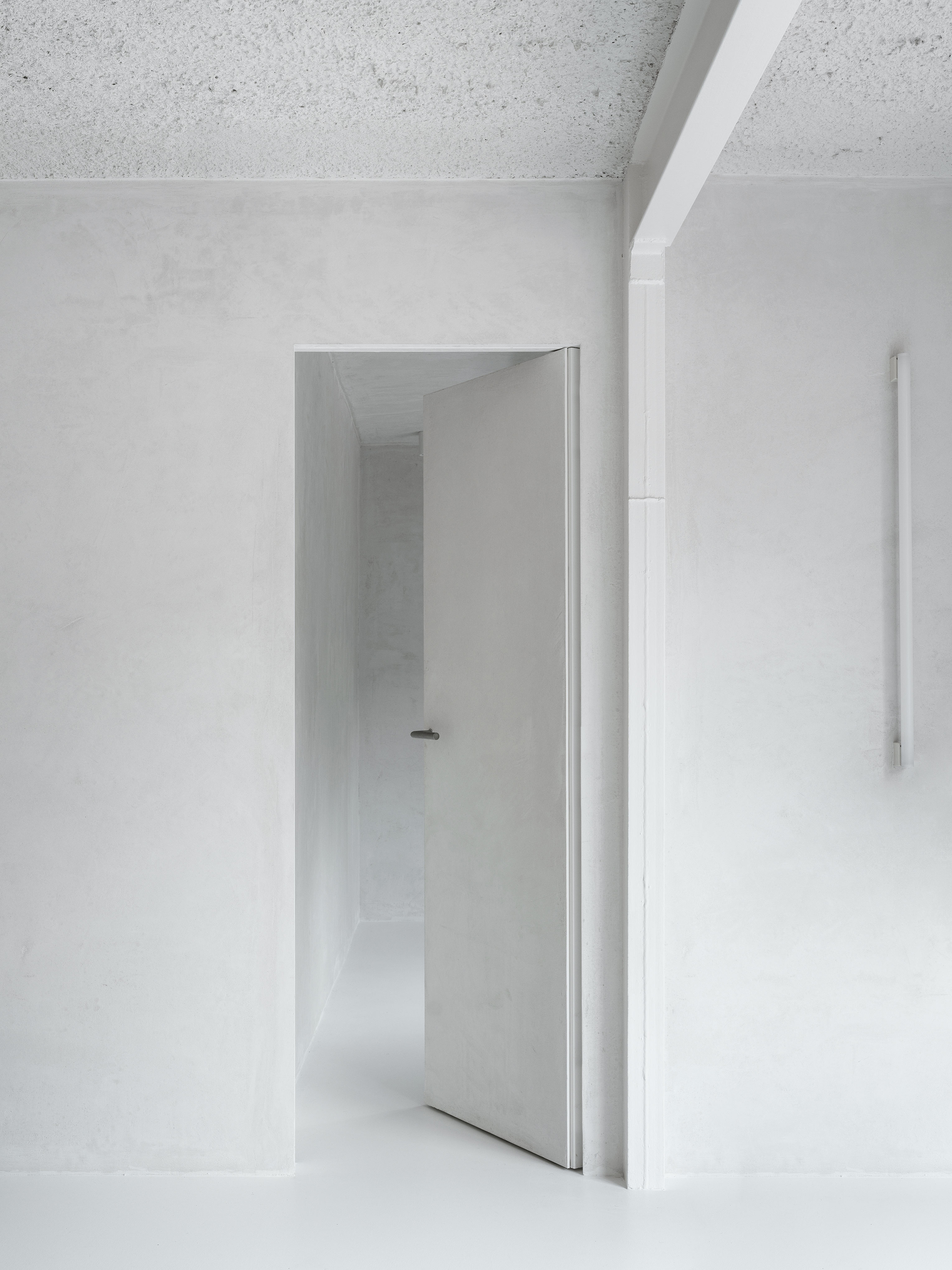 Open doorway framing a white corridor with terrazzo ceiling and continuous plaster walls