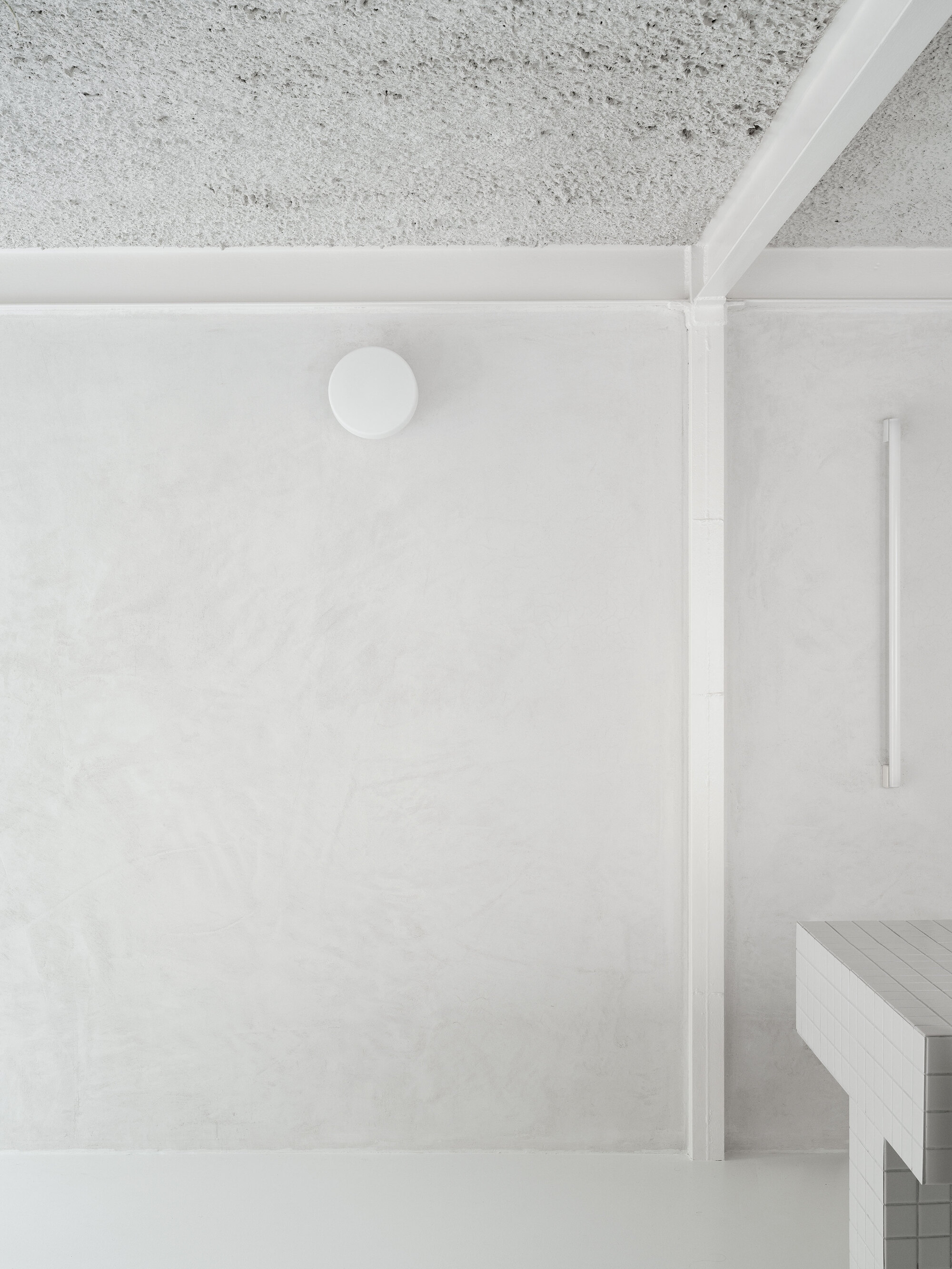 Top-down view of a white plaster ceiling with exposed concrete above and partial timber bench below
