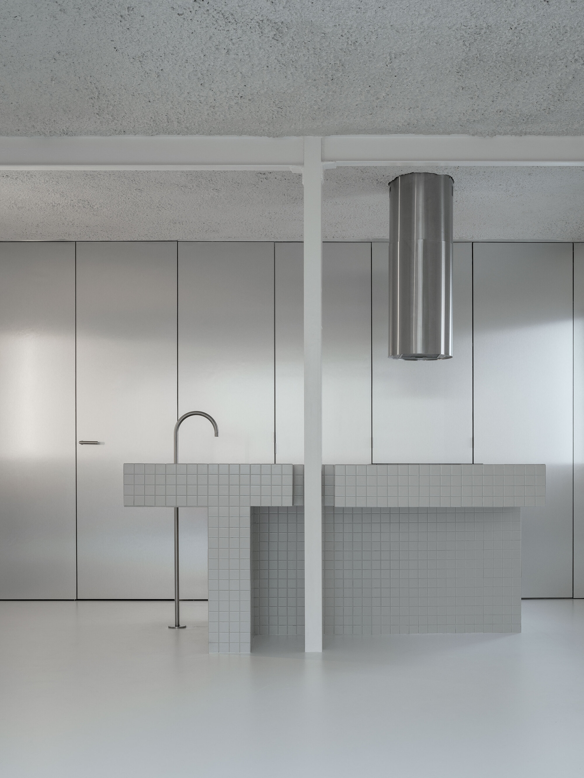 Kitchen island with white mosaic tile and stainless steel faucet beneath a cylindrical range hood