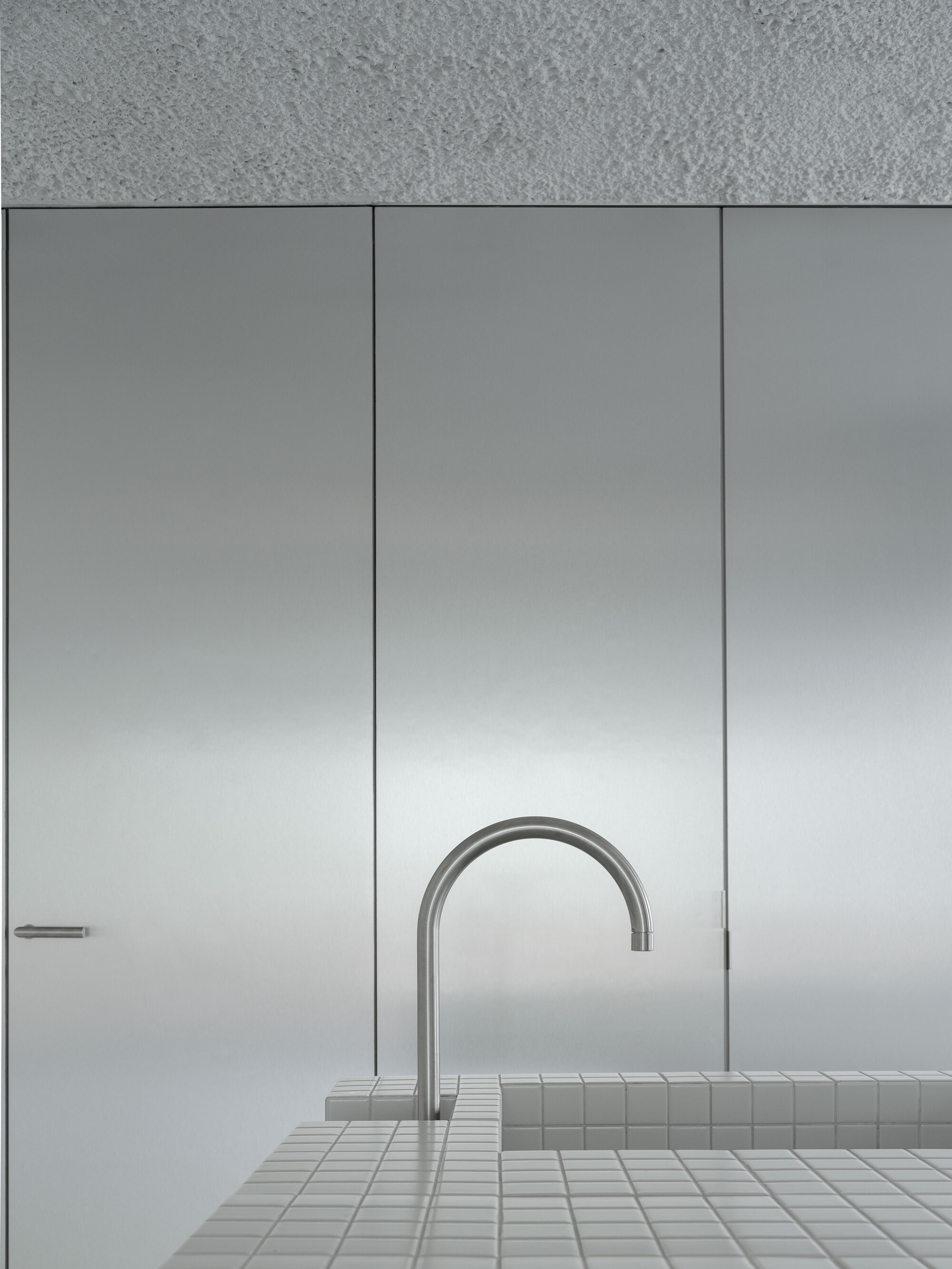 Close-up of a curved stainless steel faucet rising from a white mosaic tiled counter