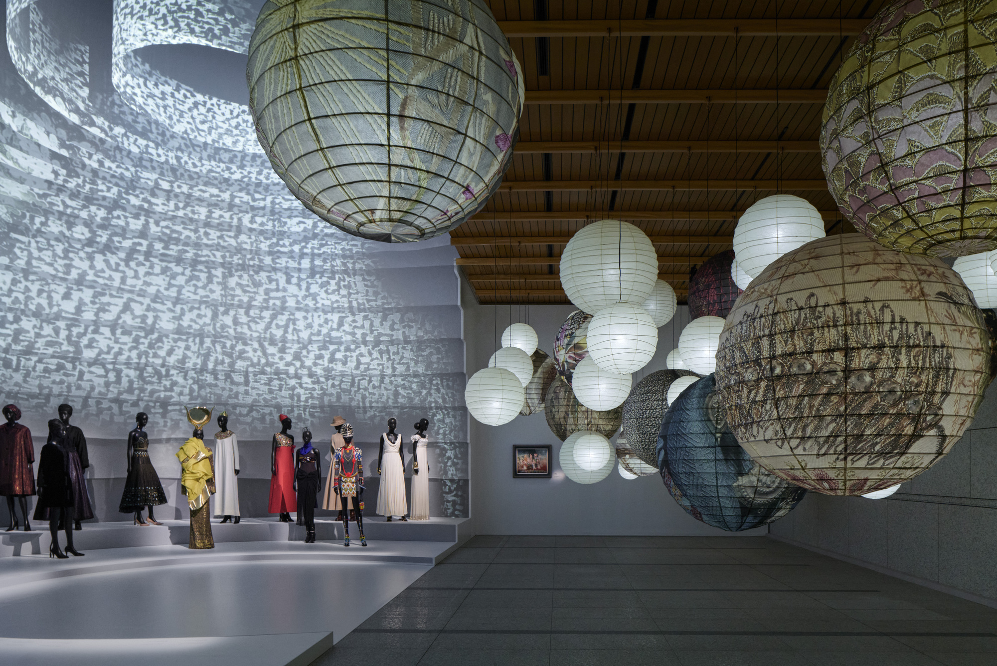 Large spherical paper lanterns hanging from a timber ceiling above a gallery with projected light patterns