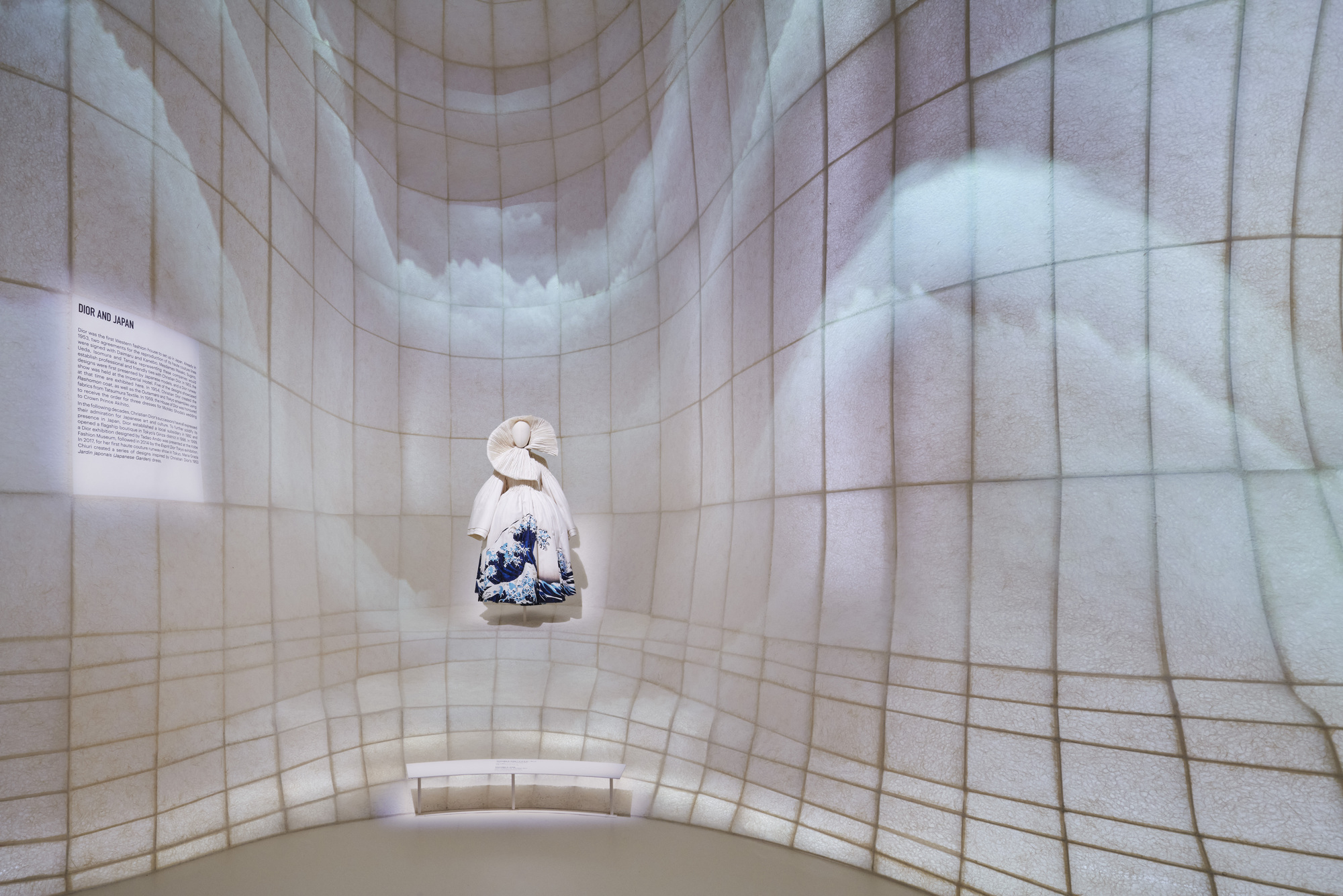 Single garment displayed in a curved alcove with projected imagery on the tiled walls