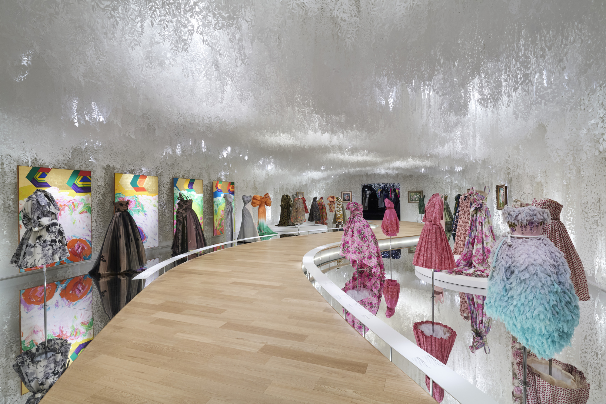 Curved exhibition platform with light wood flooring against silver foil-clad walls and colorful graphic panels