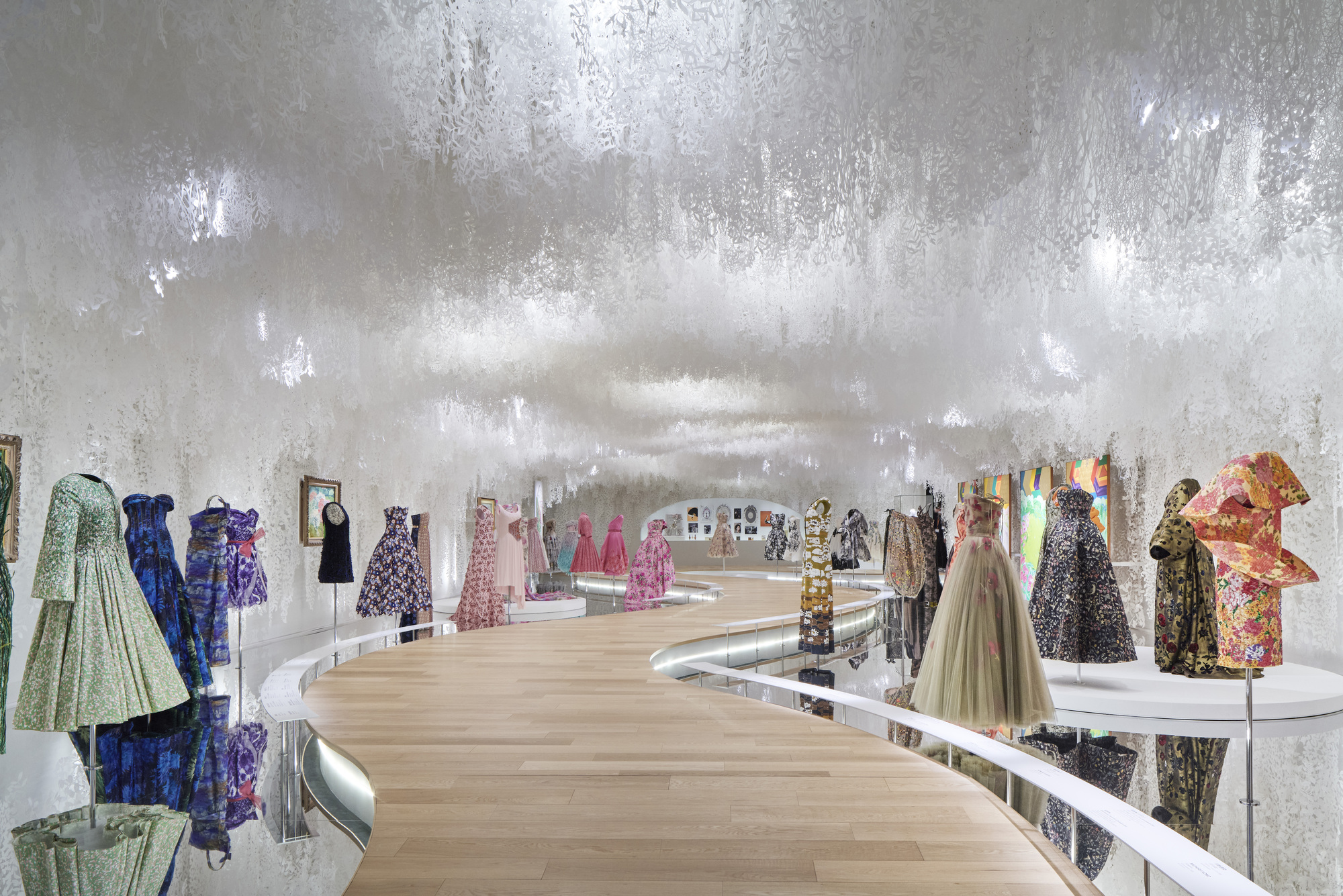 Spiraling light wood walkway through gallery space with silver textured walls and mannequins on platforms
