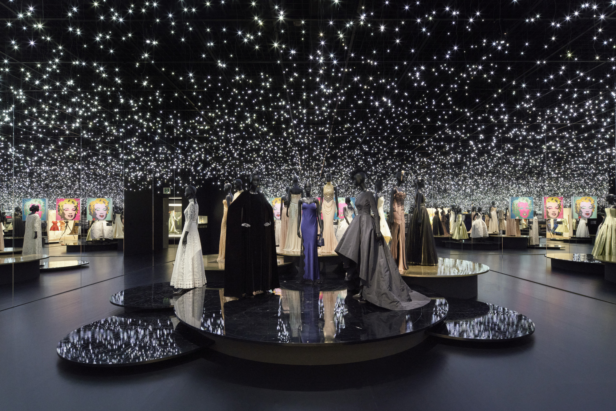 Black gallery space with circular platforms beneath a ceiling covered in thousands of small lights