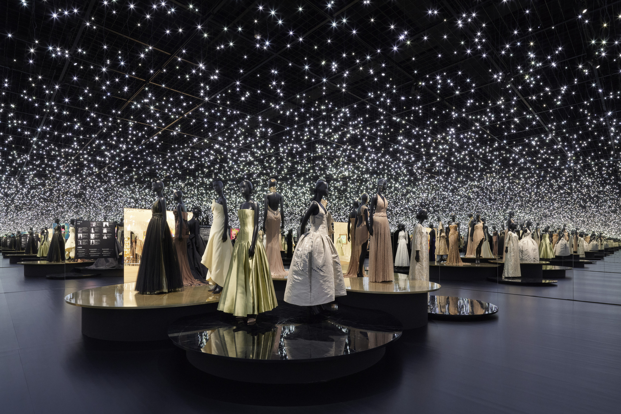 Exhibition gallery with circular display plinths and a field of suspended starlight points overhead