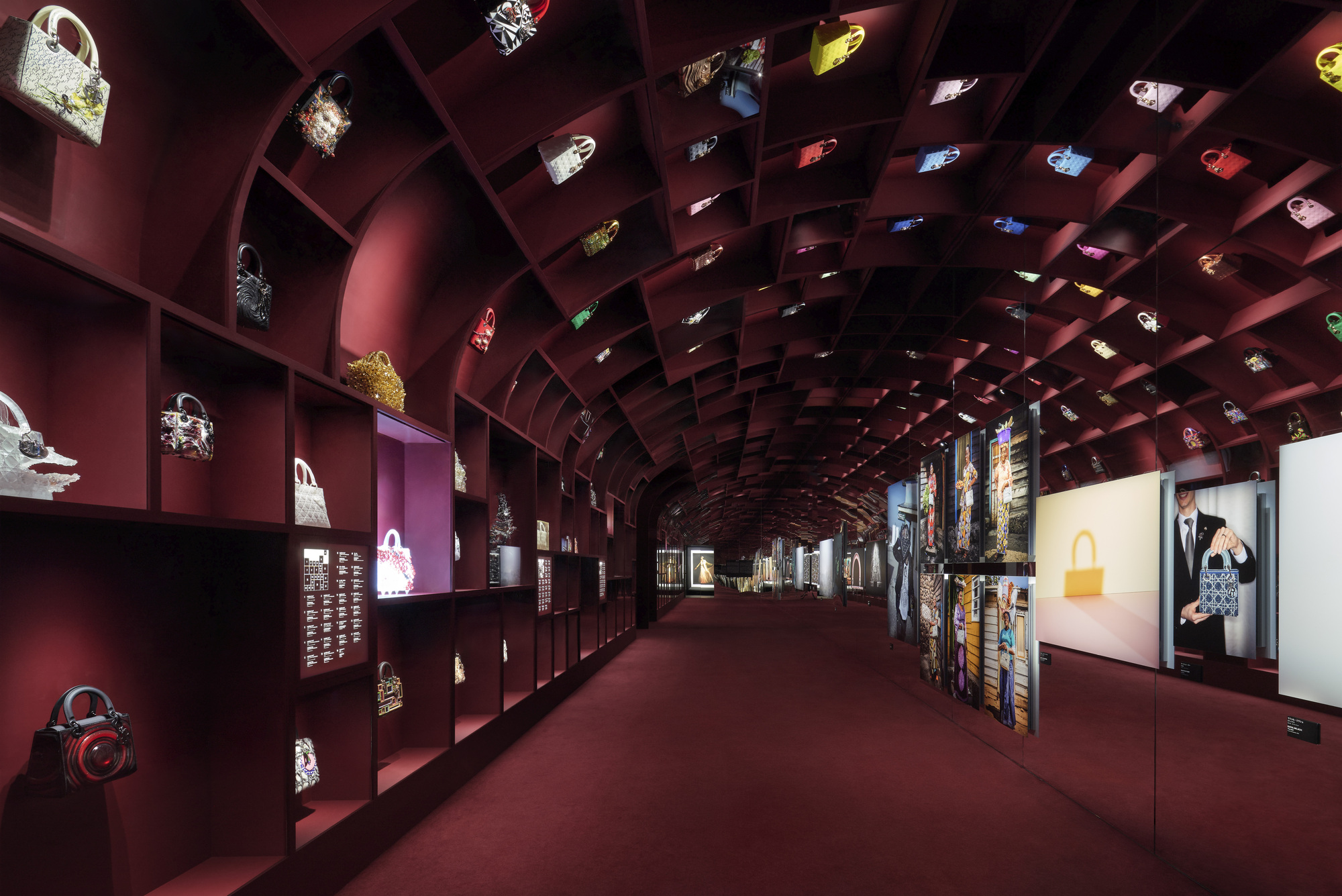 Barrel-vaulted gallery with burgundy gridded shelving displaying handbags and illuminated niches