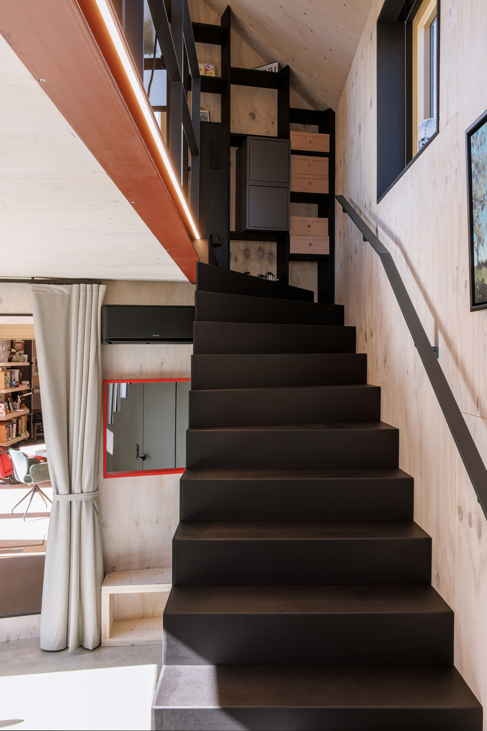 Black steel staircase with open risers ascending through a double-height space with light timber cladding