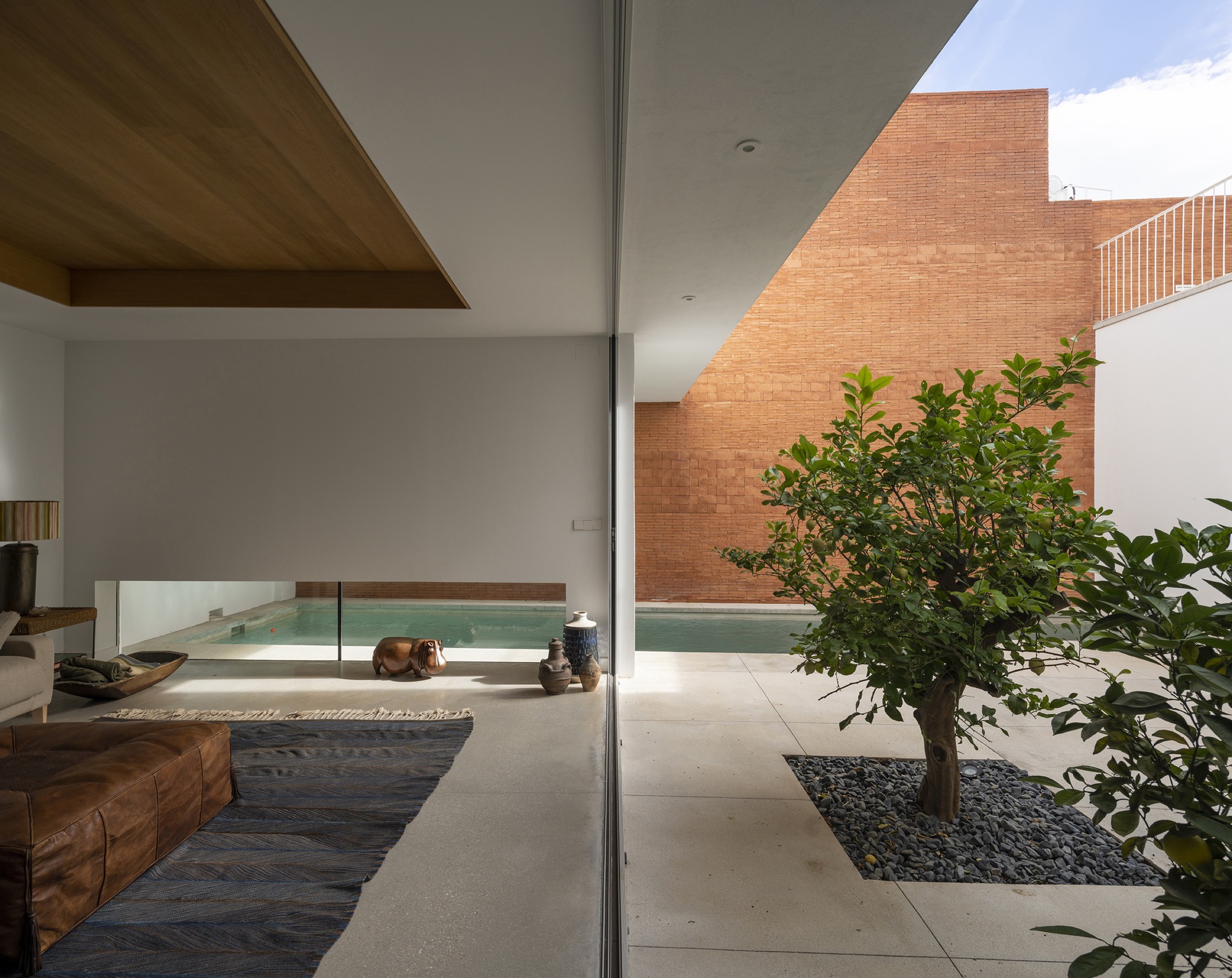 View through floor-to-ceiling glass toward the central courtyard with pool, planted tree and brick wall