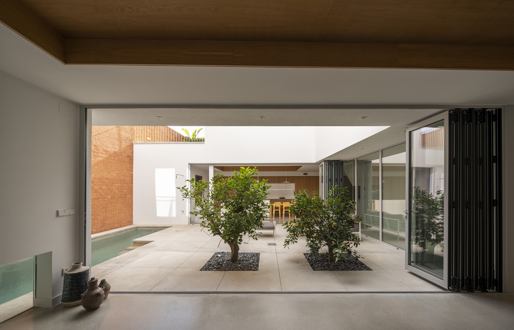 Interior view through folding glass doors to courtyard with two planted trees on concrete pavers
