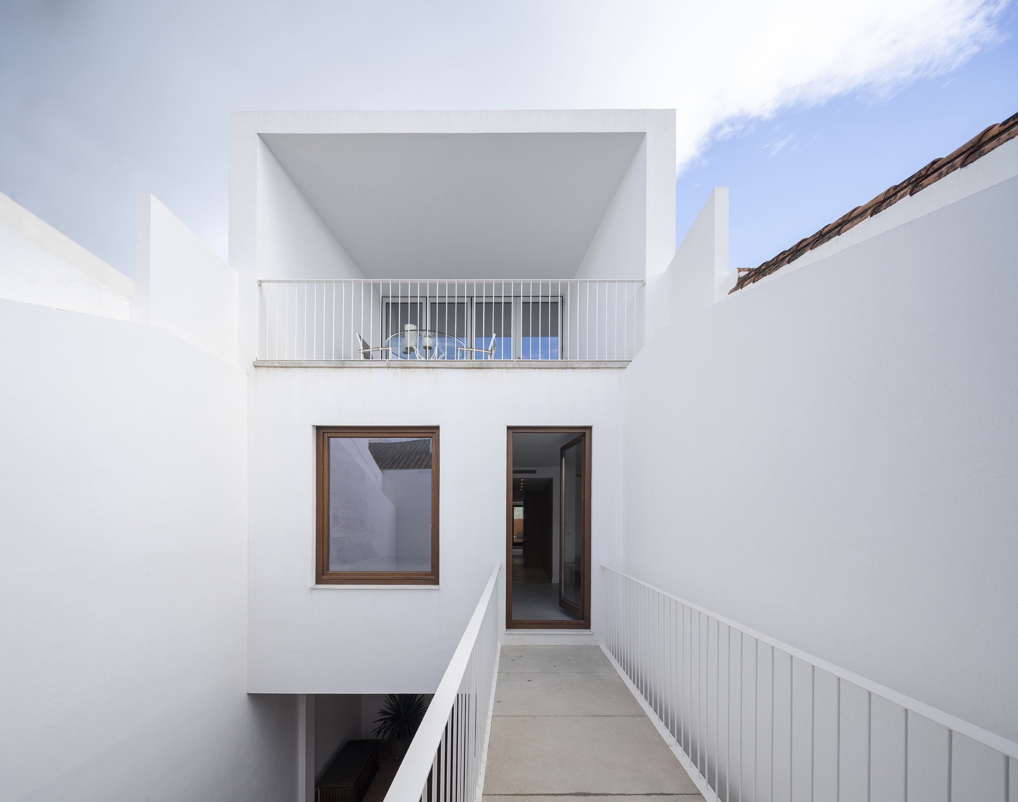 White rendered courtyard passage with upper balcony and metal railings under bright midday sun
