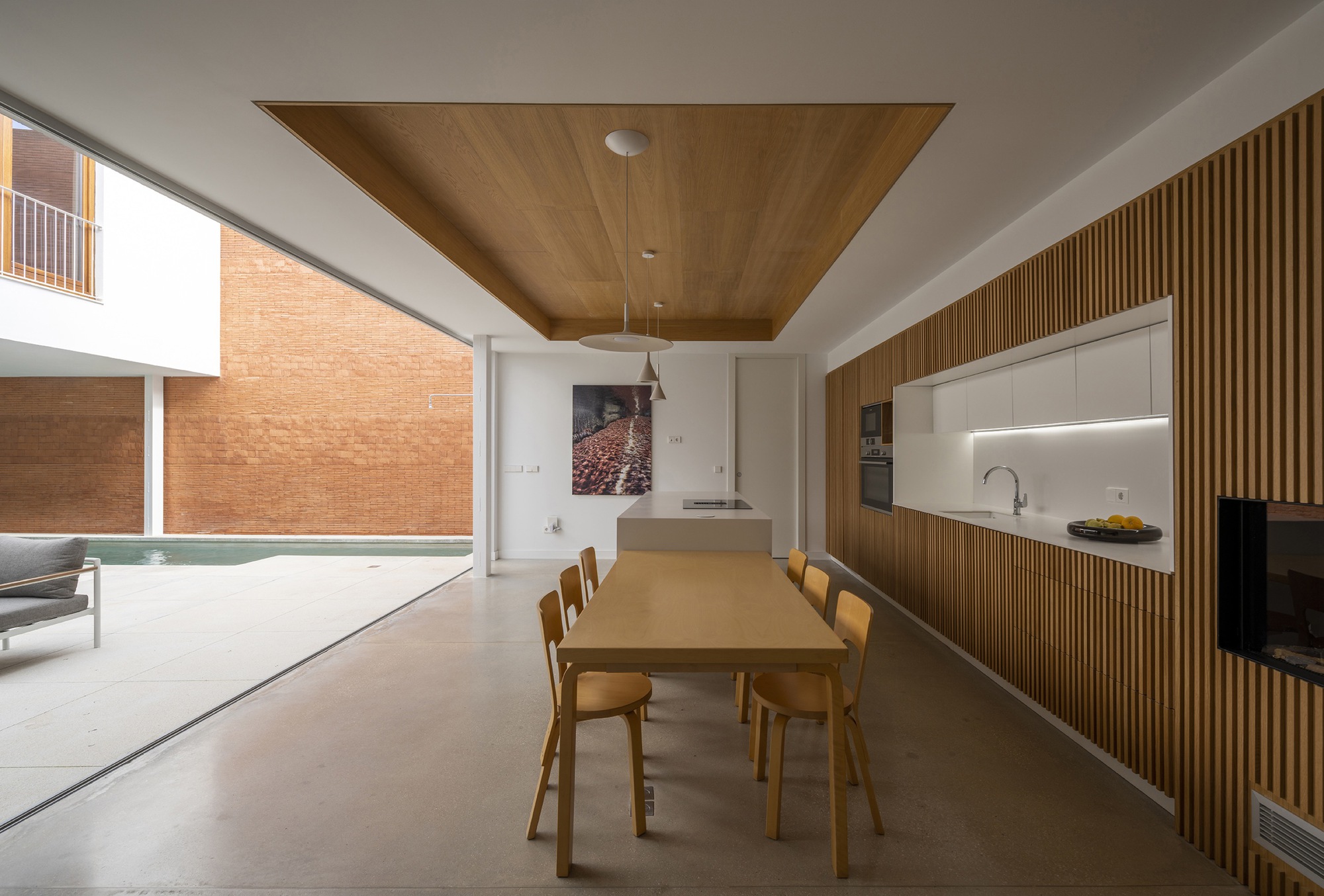 Open-plan dining space with timber ceiling panel and slatted wood kitchen cabinetry overlooking the courtyard