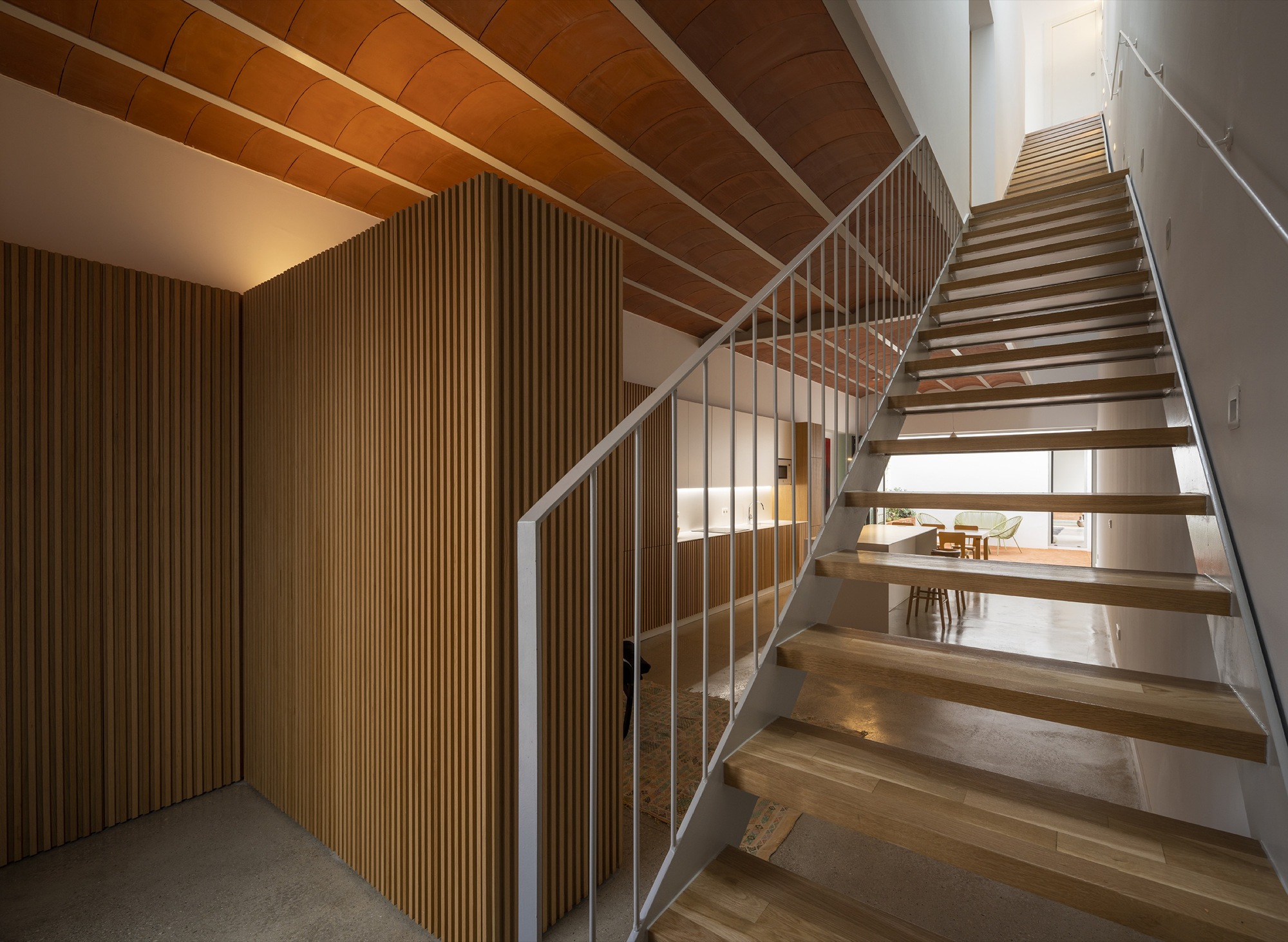 Timber staircase with glass railing and vertical wood slat partition beneath a vaulted ceiling