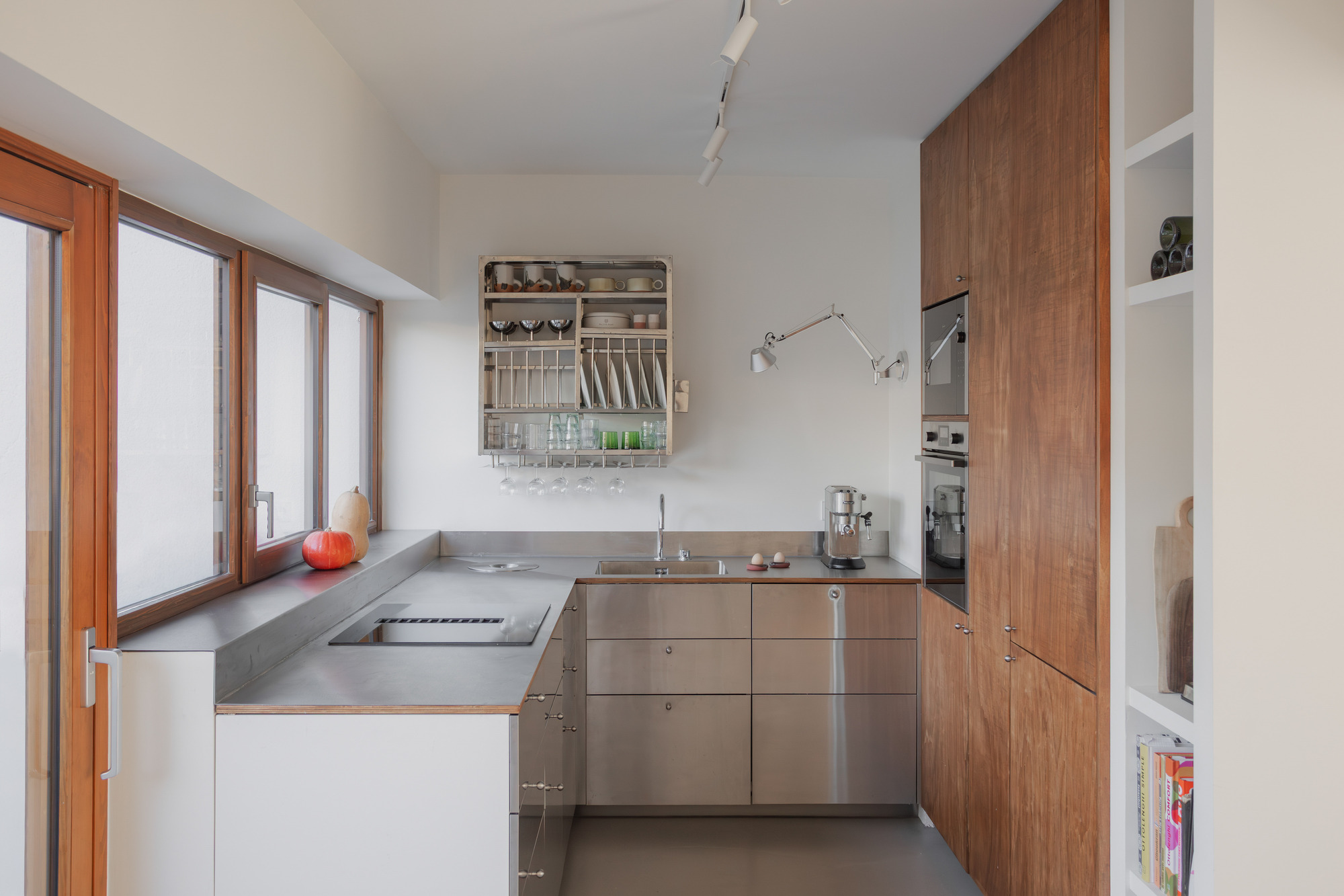 Compact kitchen with stainless steel countertops, timber cabinetry and a tall window overlooking the garden