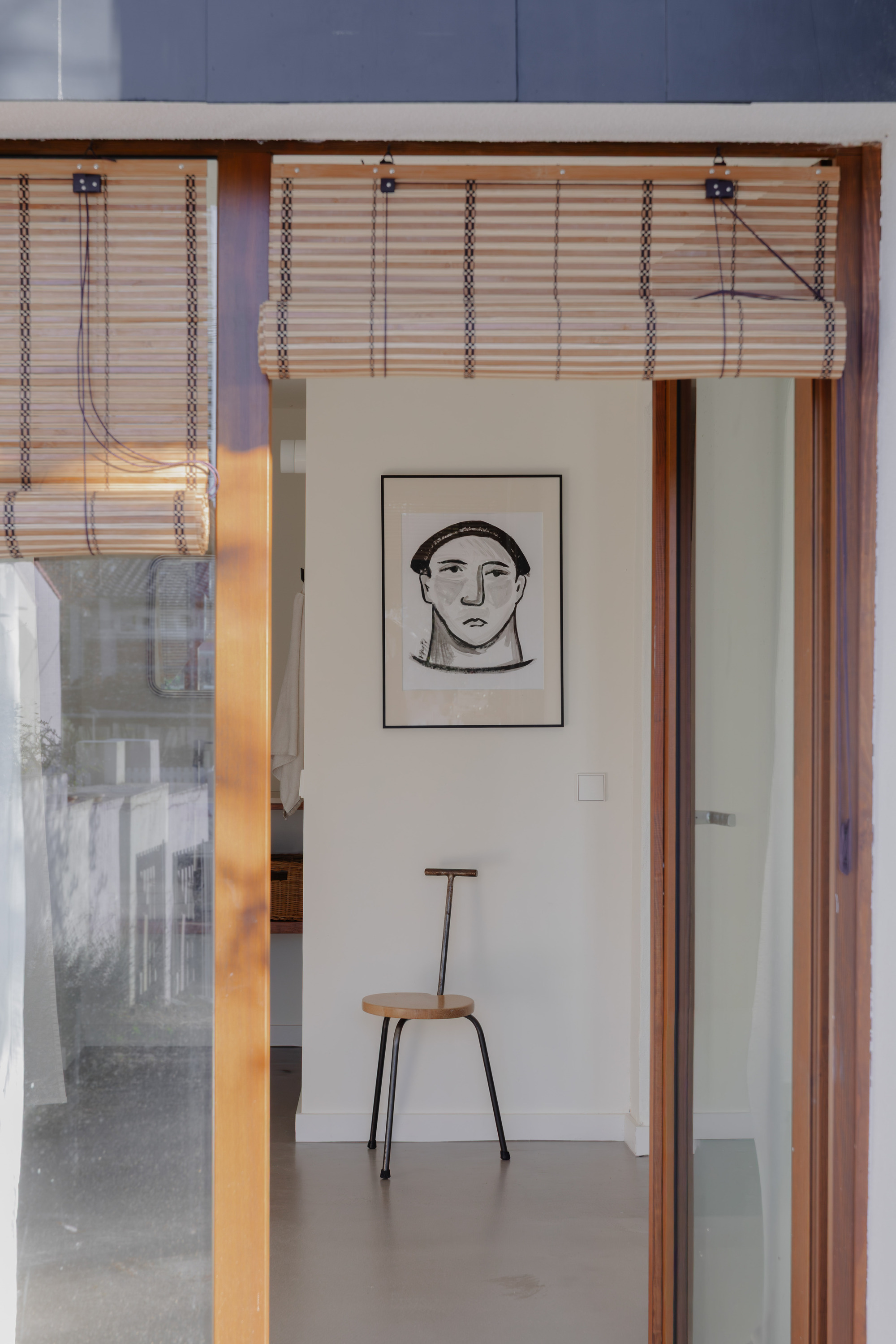 Timber framed doorway with woven bamboo blind leading into a room with a framed portrait and chair