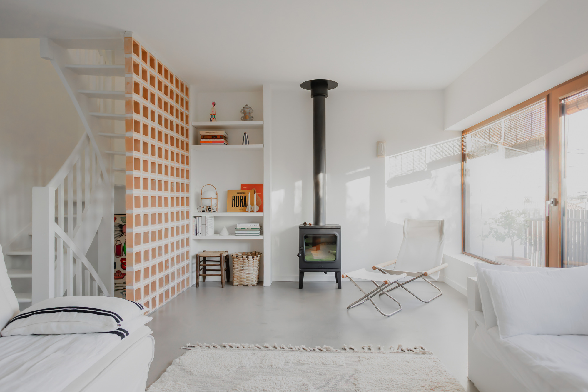 Open plan interior with freestanding black wood stove and timber grid partition beside white painted staircase