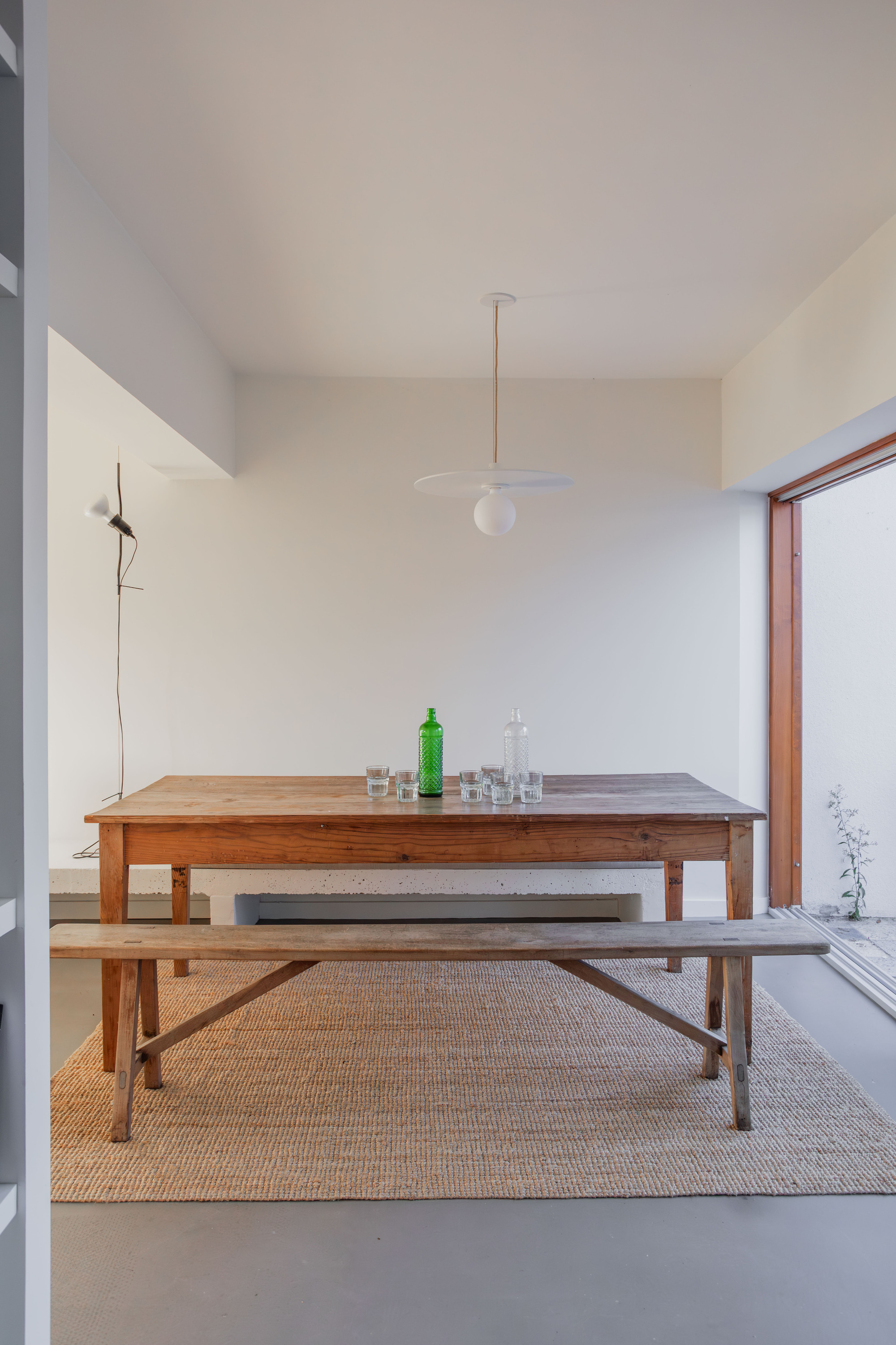 Dining area with timber table and benches beneath a pendant light beside a courtyard window