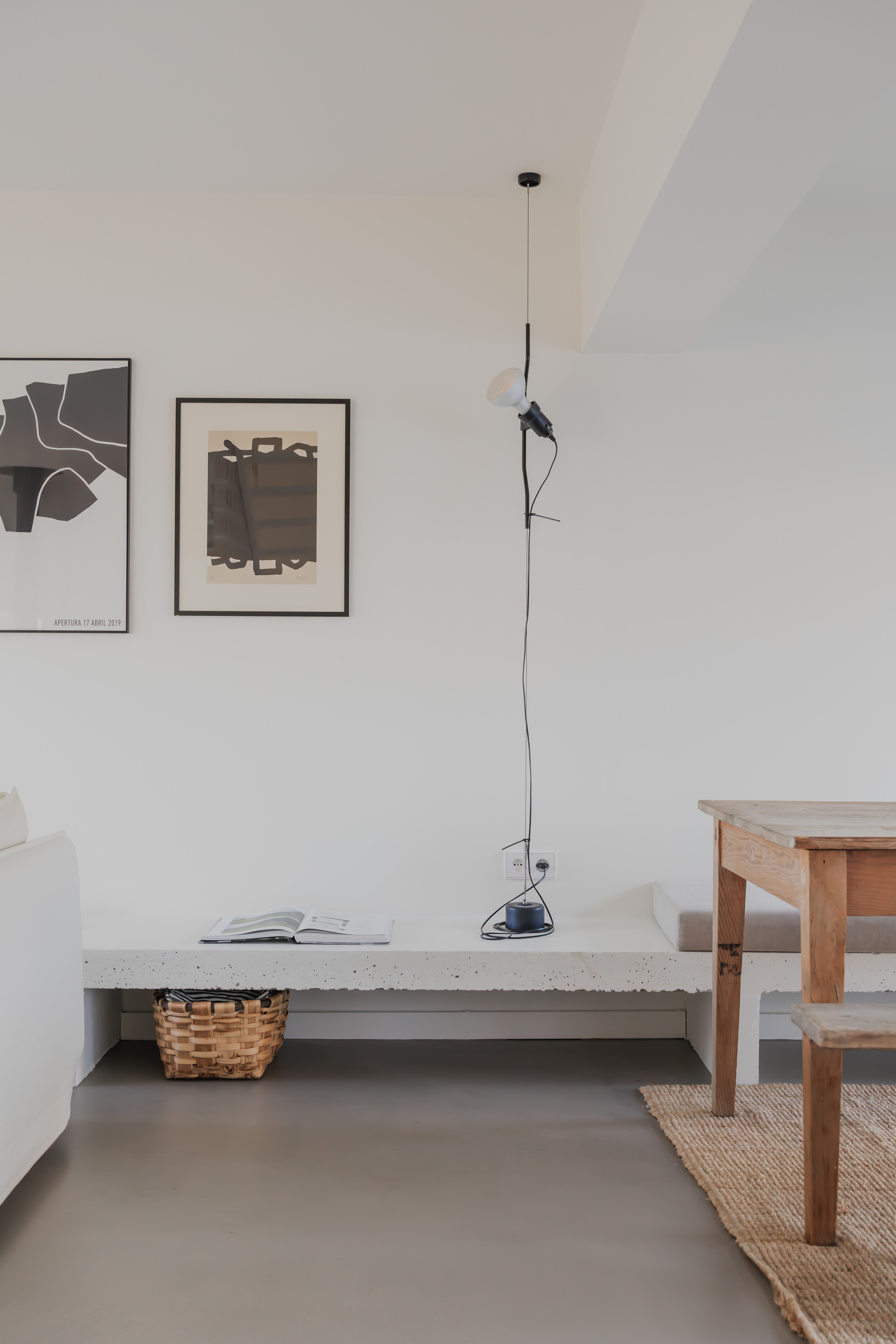 Living area with concrete bench, pendant lamp, framed artworks on white walls and grey polished floor