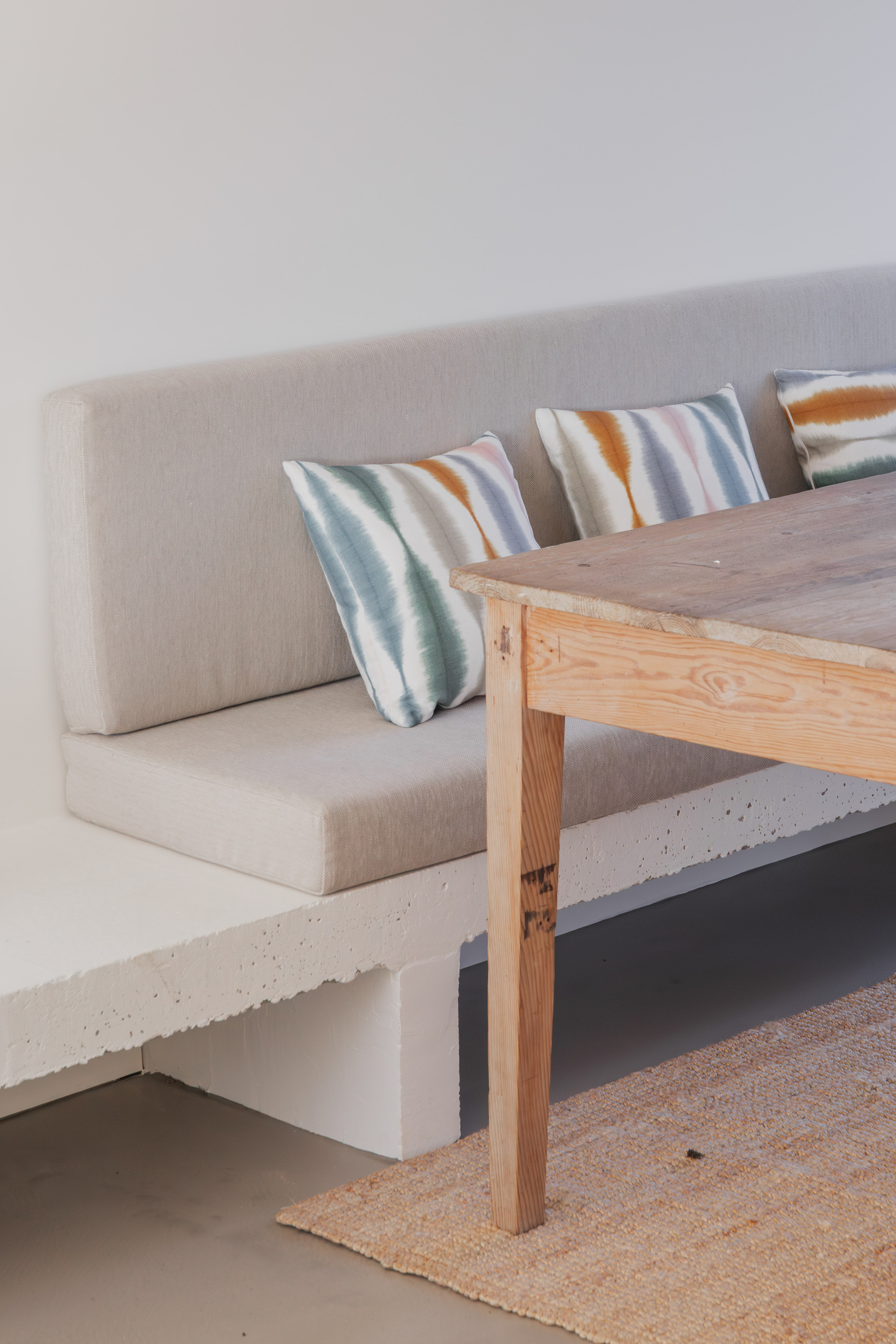 Built-in concrete bench with upholstered seating and striped cushions beneath timber dining table