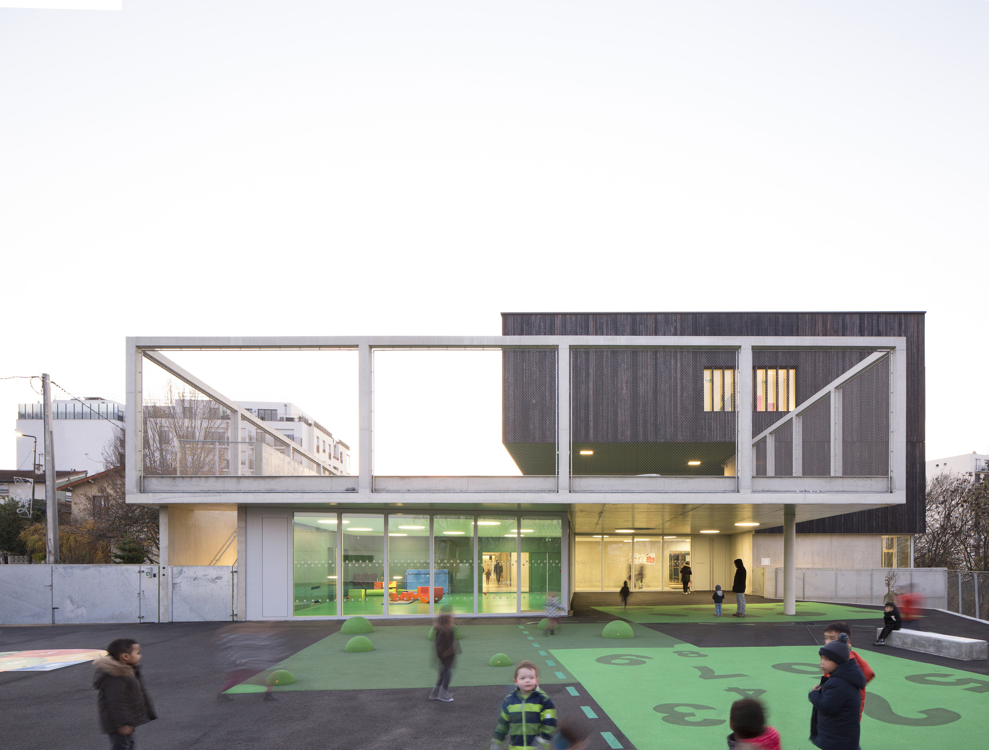Two-storey facade with timber cladding above glazed ground floor and green play surface with children