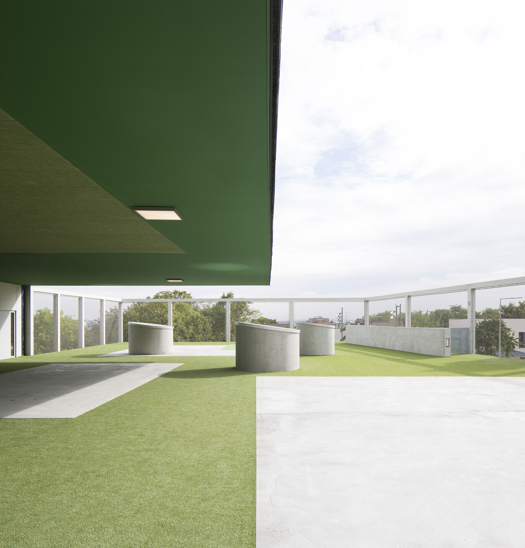 Covered terrace with green soffit and cylindrical concrete volumes on artificial turf under overcast skies