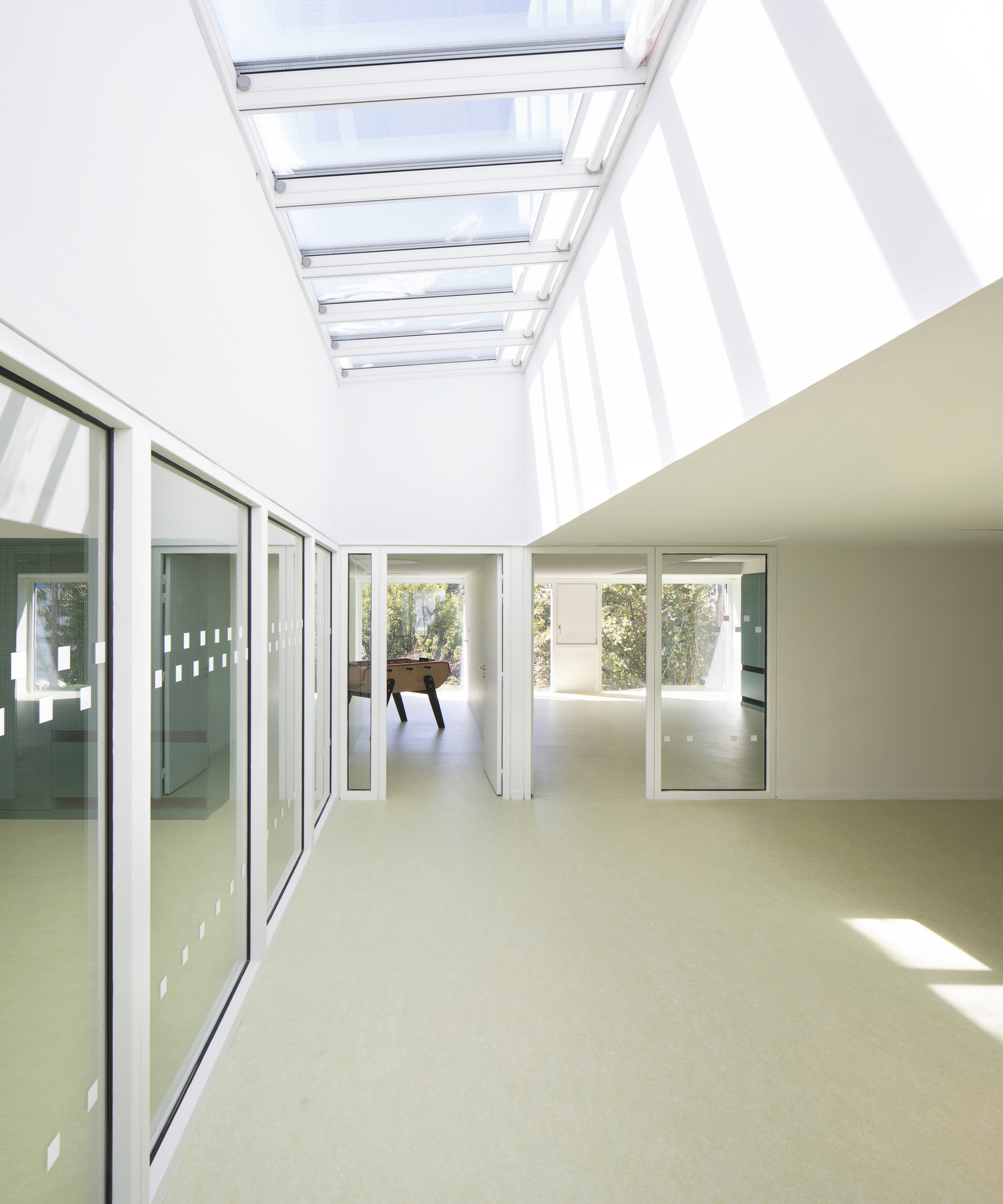 Skylit corridor with glazed walls connecting interior spaces with sunlight filtering through overhead louvers