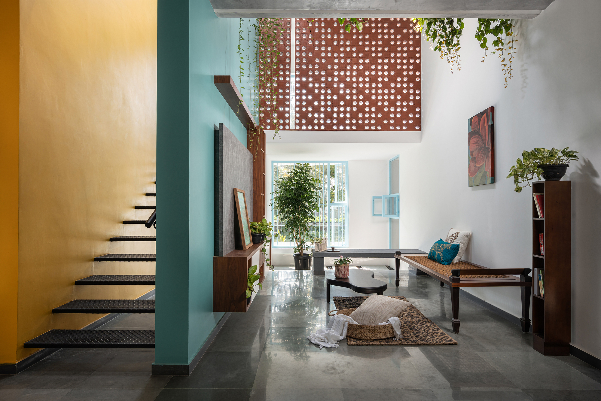 Double-height living room with perforated screen above and staircase beside yellow ochre wall