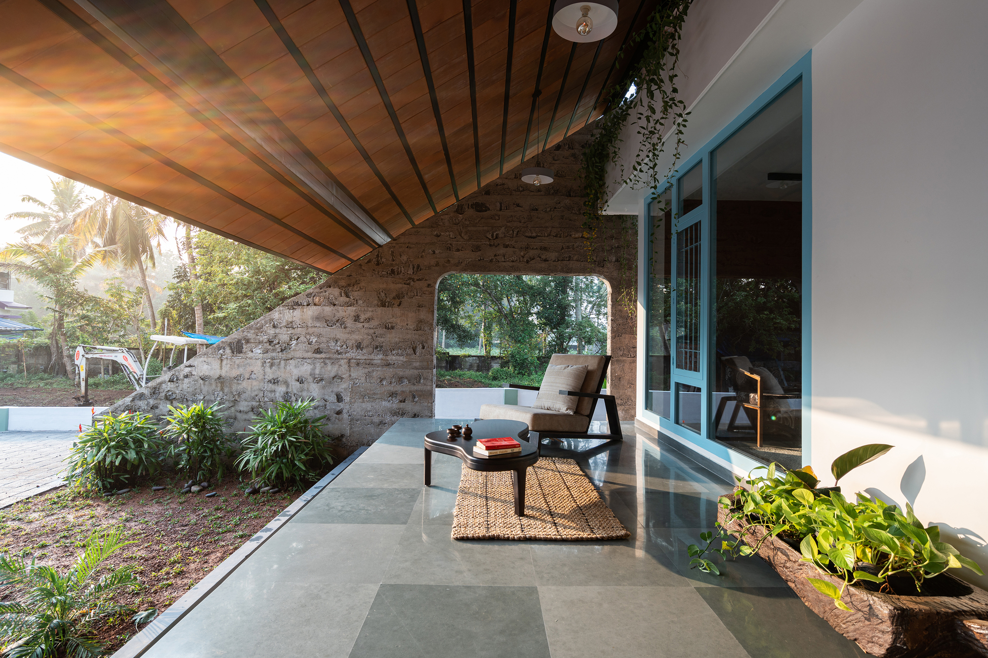 Covered porch with exposed wood ceiling, laterite stone wall and planted beds flanking glass doors