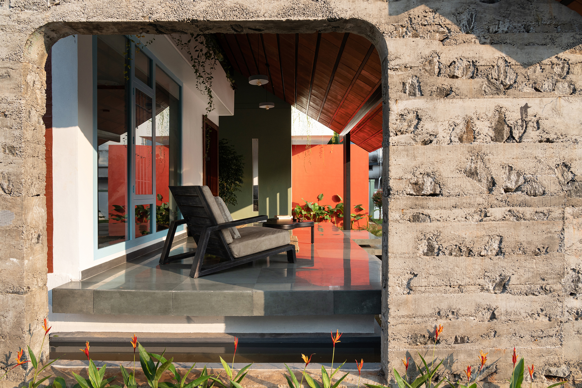 Arched opening in laterite wall framing seating area with polished concrete floor and bird-of-paradise plantings