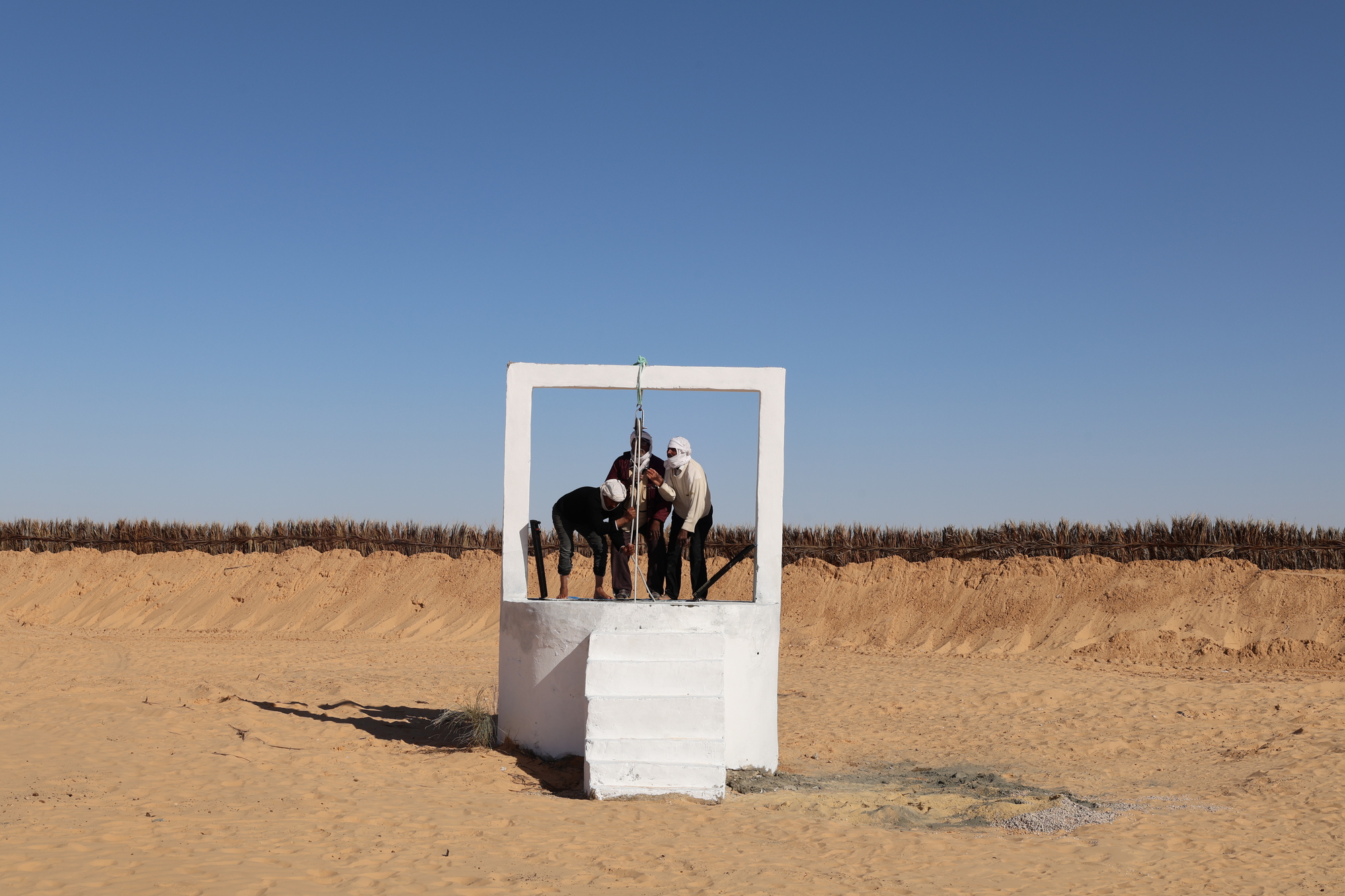 Workers installing equipment within a white painted concrete portal frame standing in the desert sand