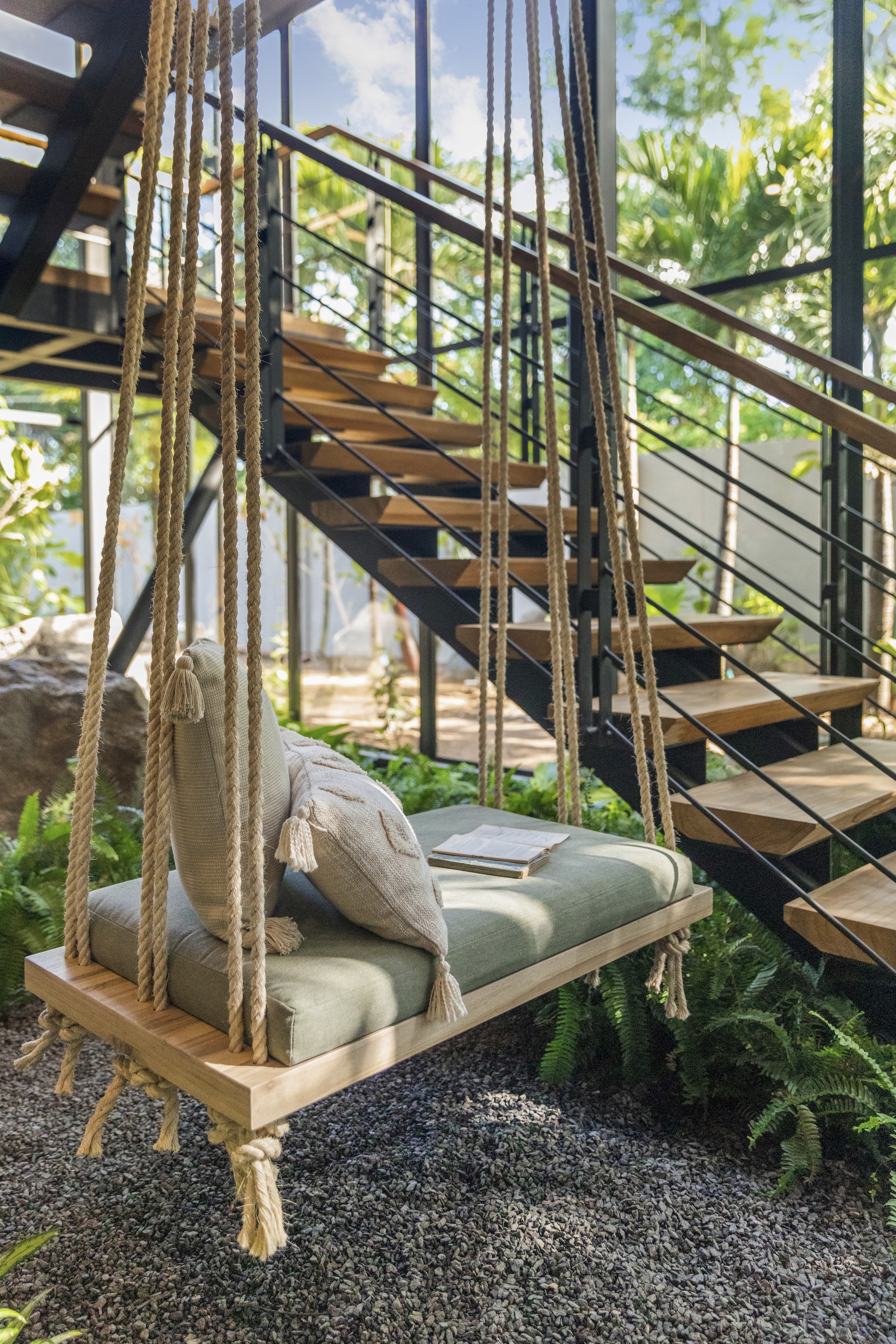 Rope-suspended swing beneath an open-tread steel and timber staircase with ferns
