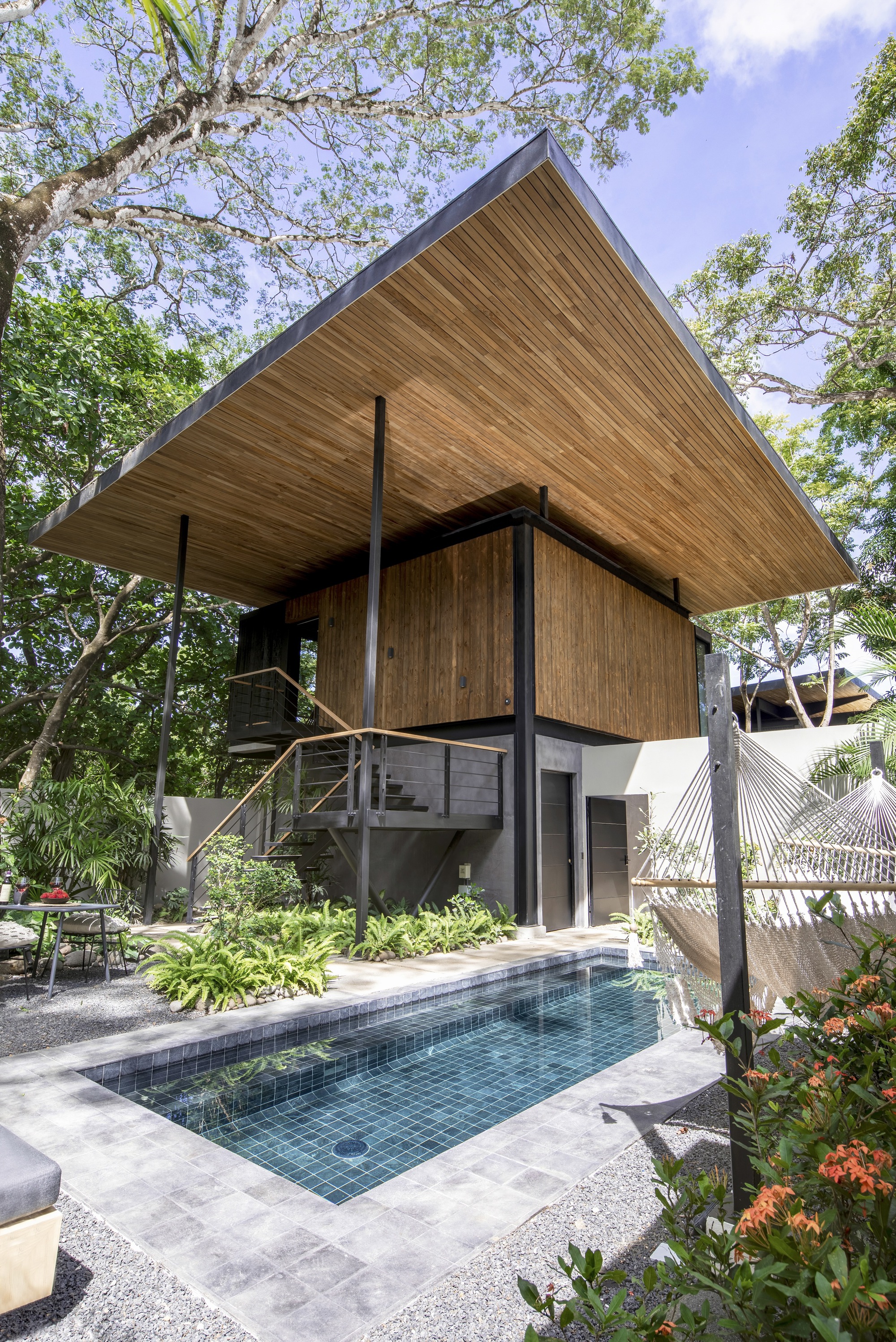 Poolside view of the cantilevered timber-clad volume with gabled soffit and steel columns