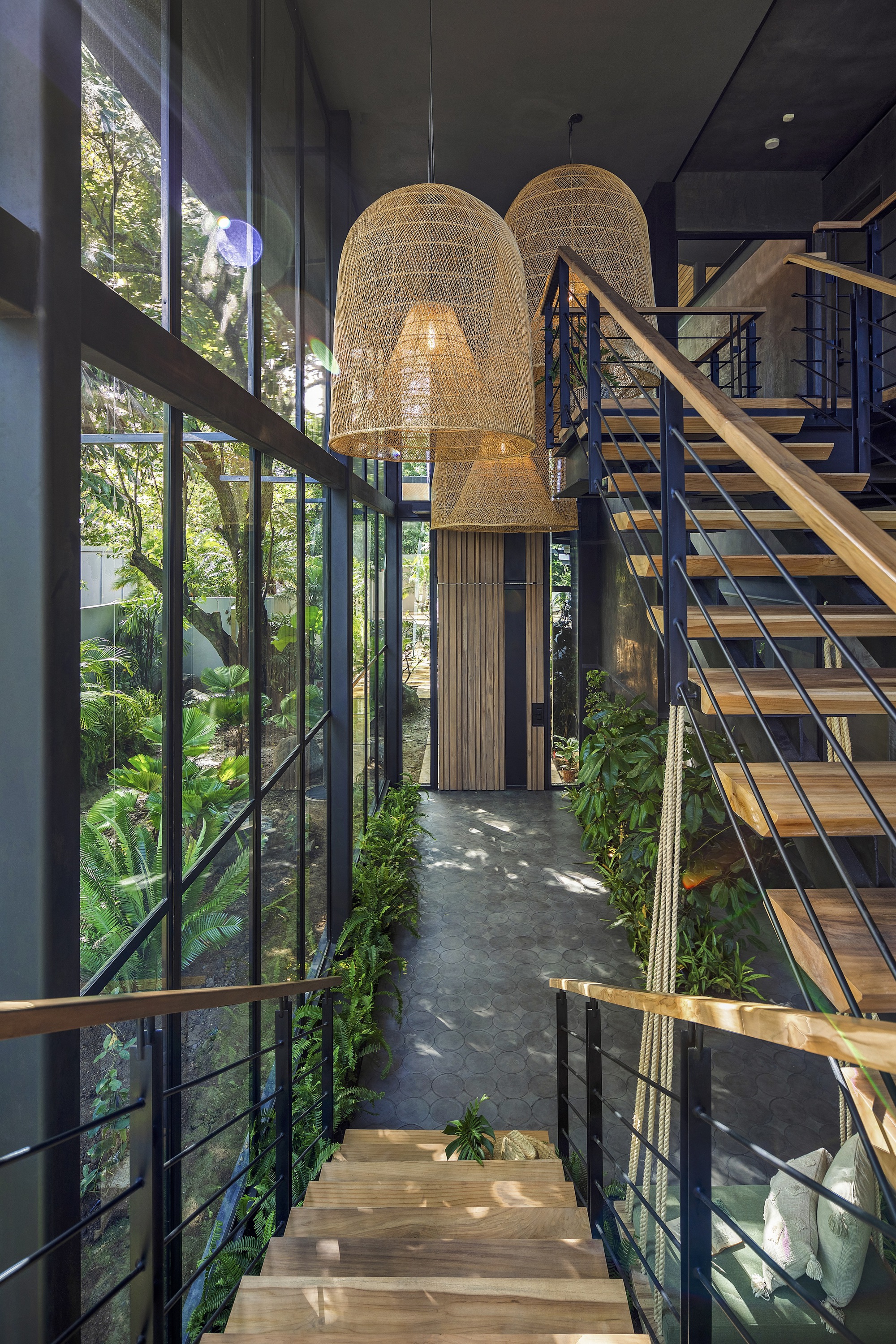 Double-height entry hall with woven pendant lights and metal staircase overlooking planted courtyard
