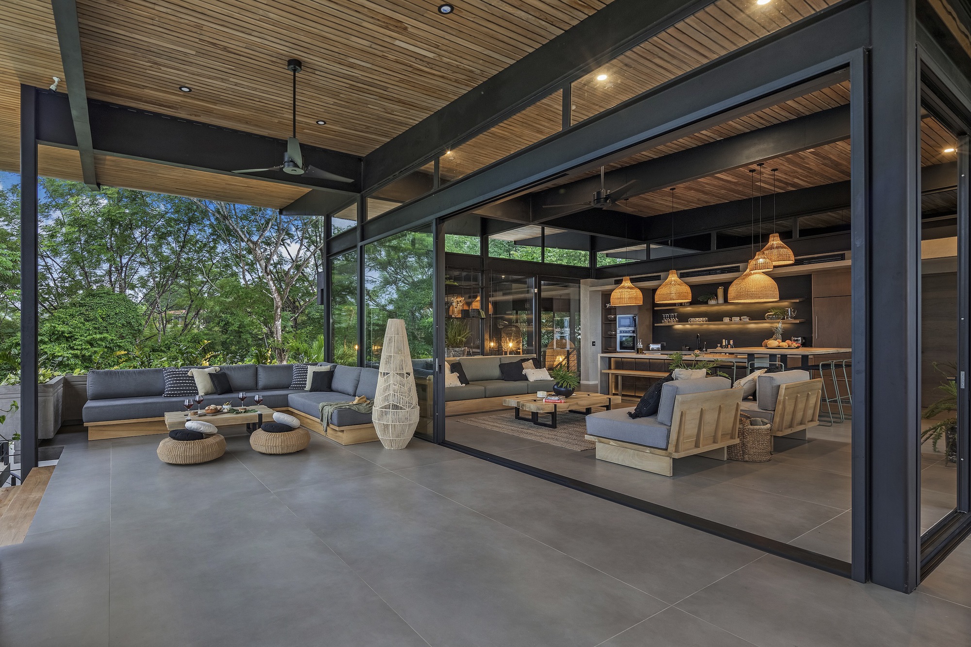 Covered terrace with steel frame opening to living spaces and garden at dusk