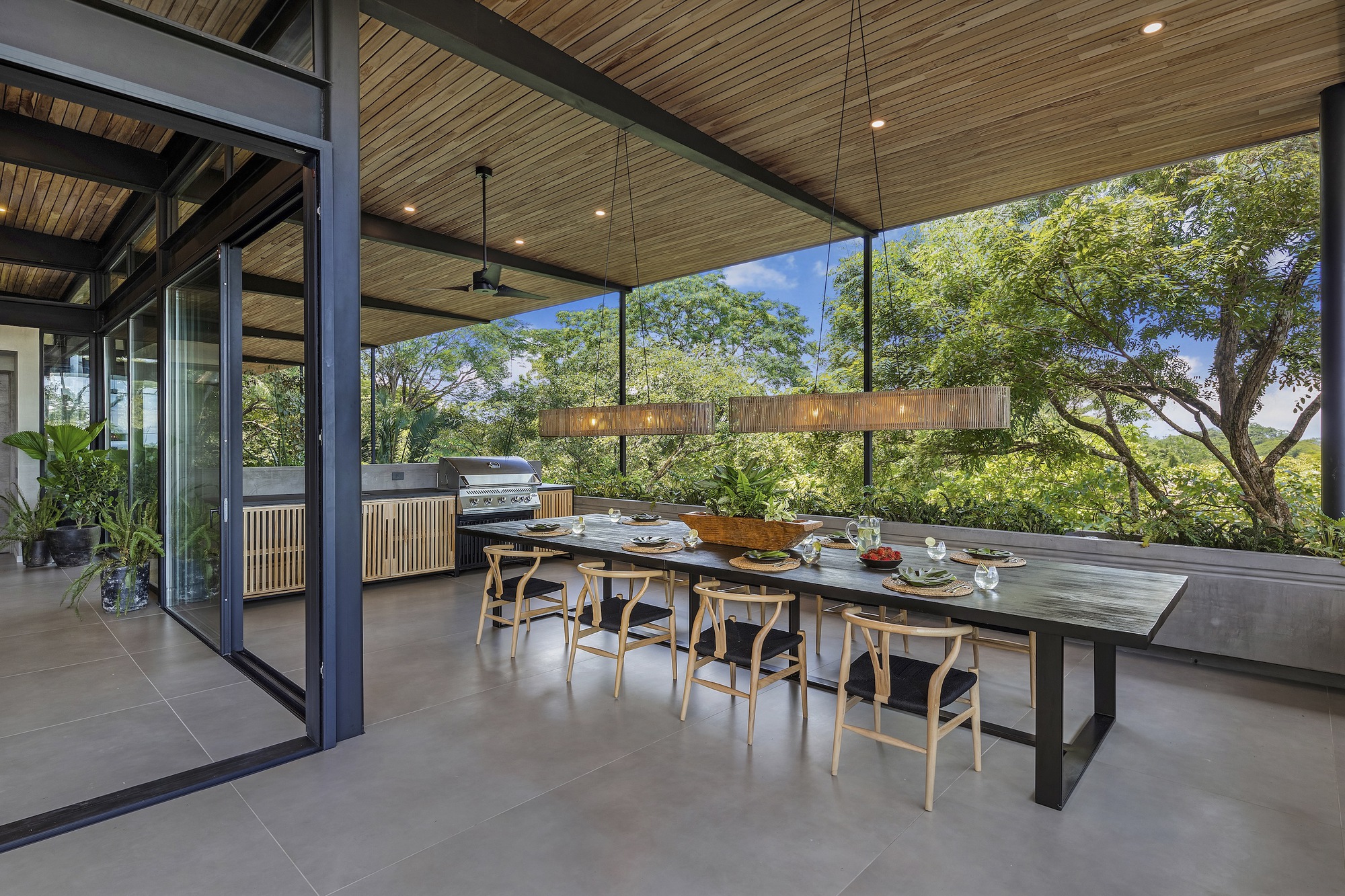 Outdoor dining terrace beneath a deep roof overhang with views to surrounding trees